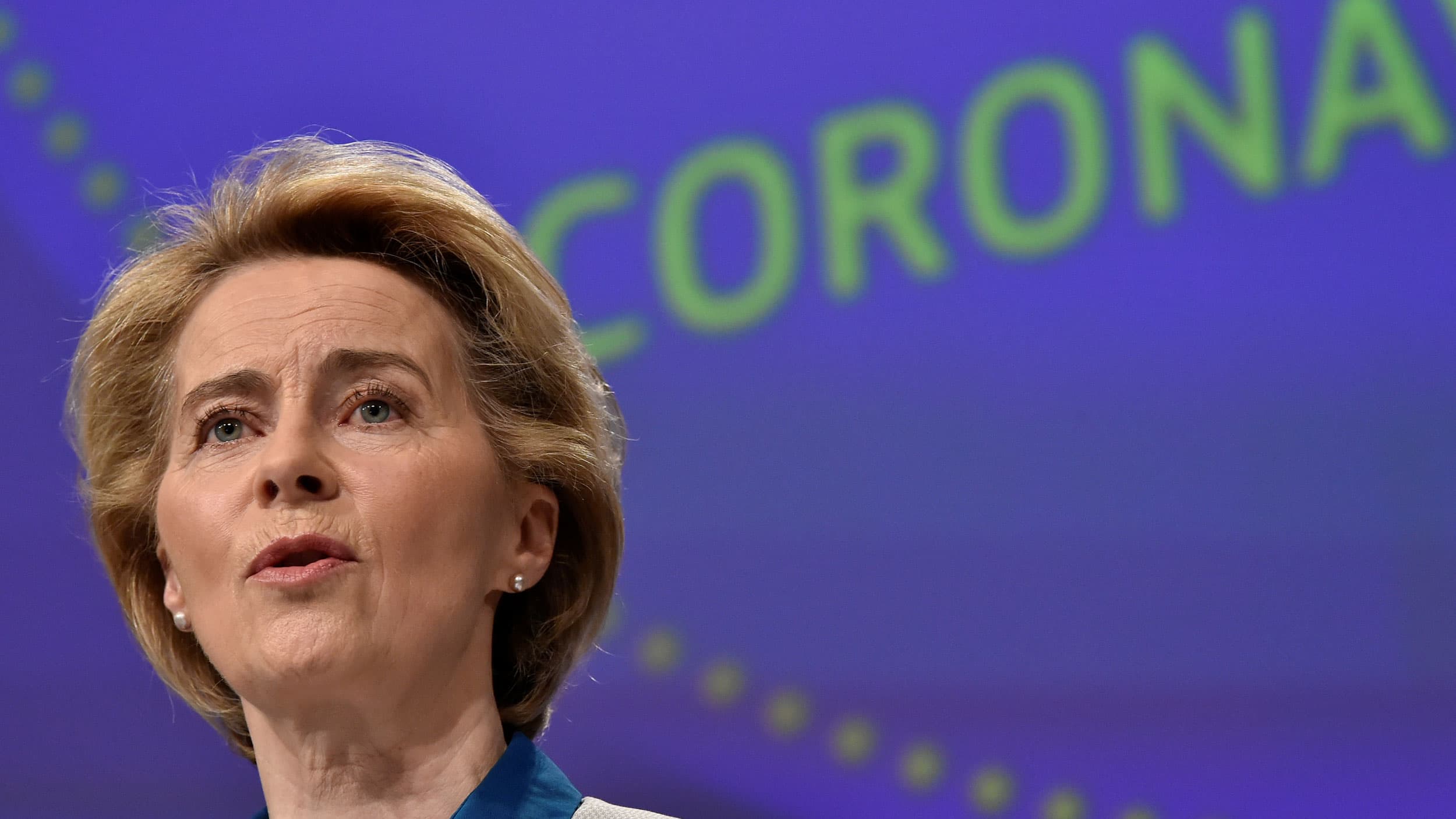 The President of European Commission Ursula von der Leyen is shown in a close up photograph wearing pearl earings and the word "coronavirus" in the background.