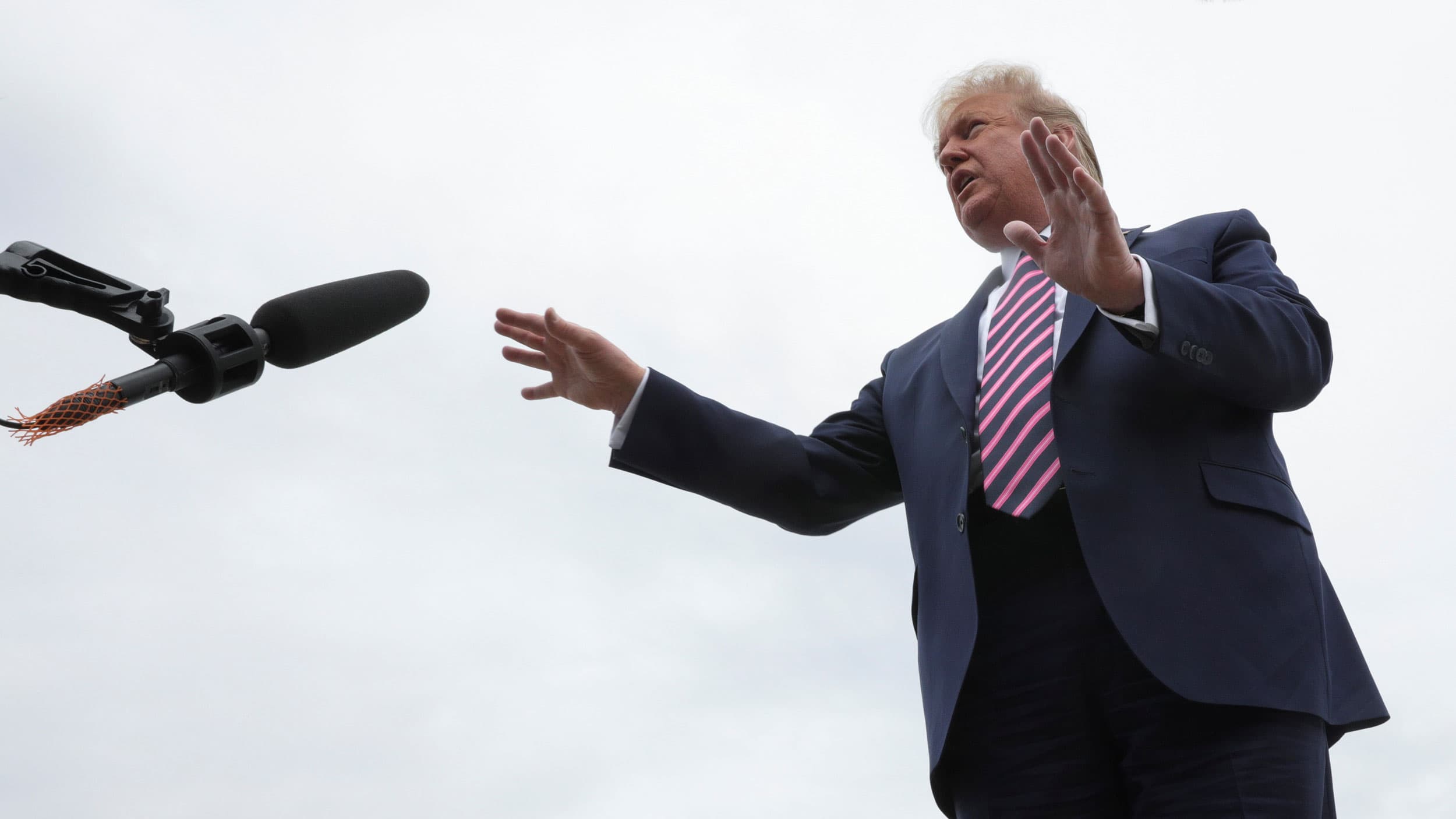 US President Donald Trump is shown with his hands out stretched and wearing a dark blue suit with a pinked striped tie.