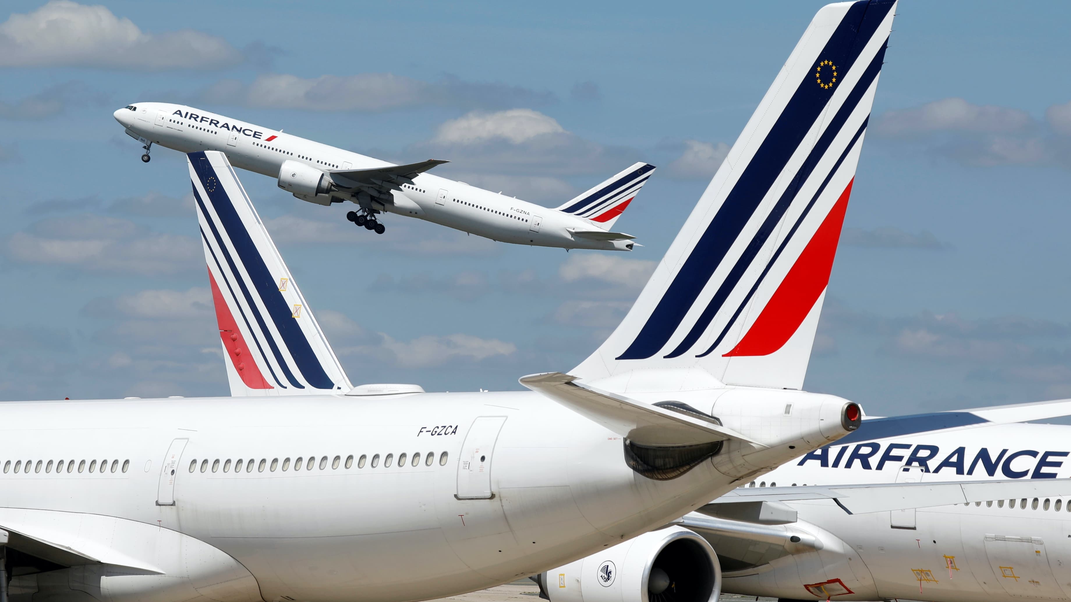 Three Air France white airplanes at the airport, one in the air