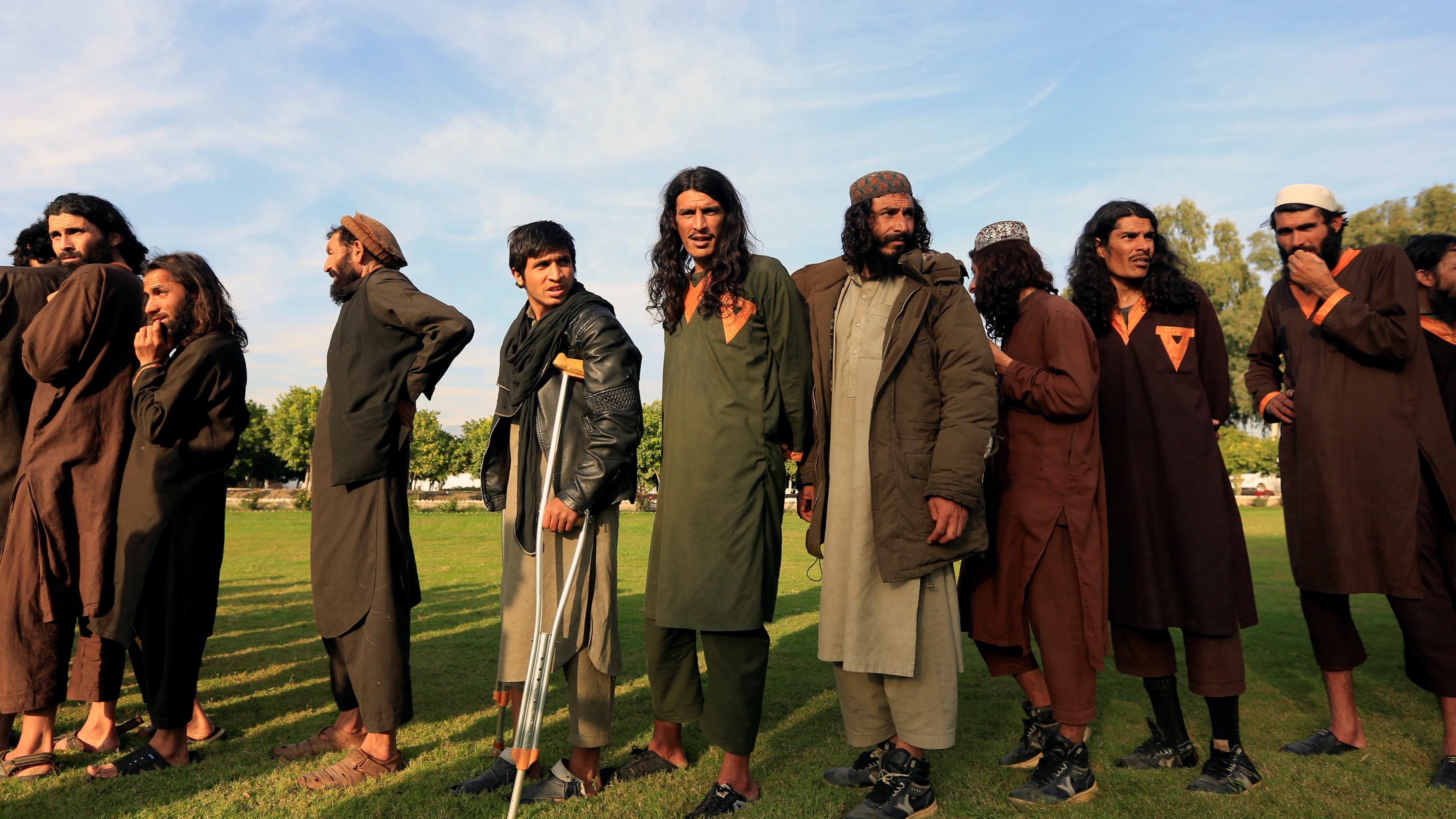 A group of men stand in a row in green grass under a blue sky.
