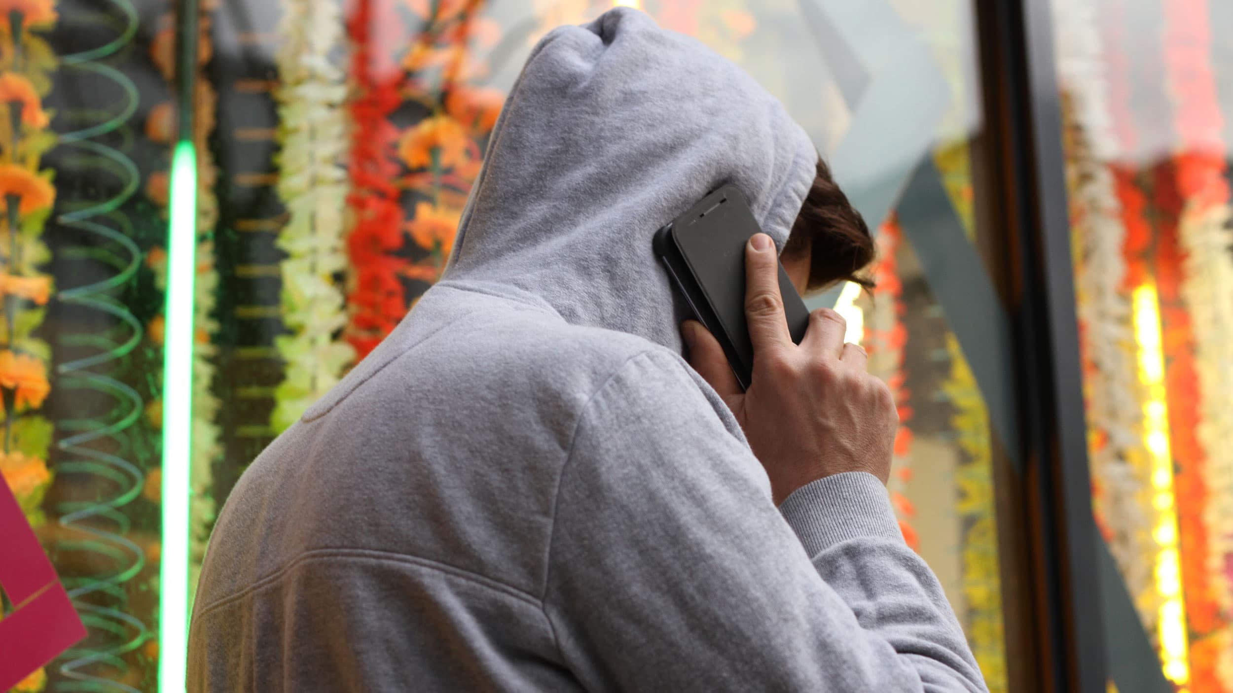 A person in a hoodie turned away from the camera speaks on a cell phone