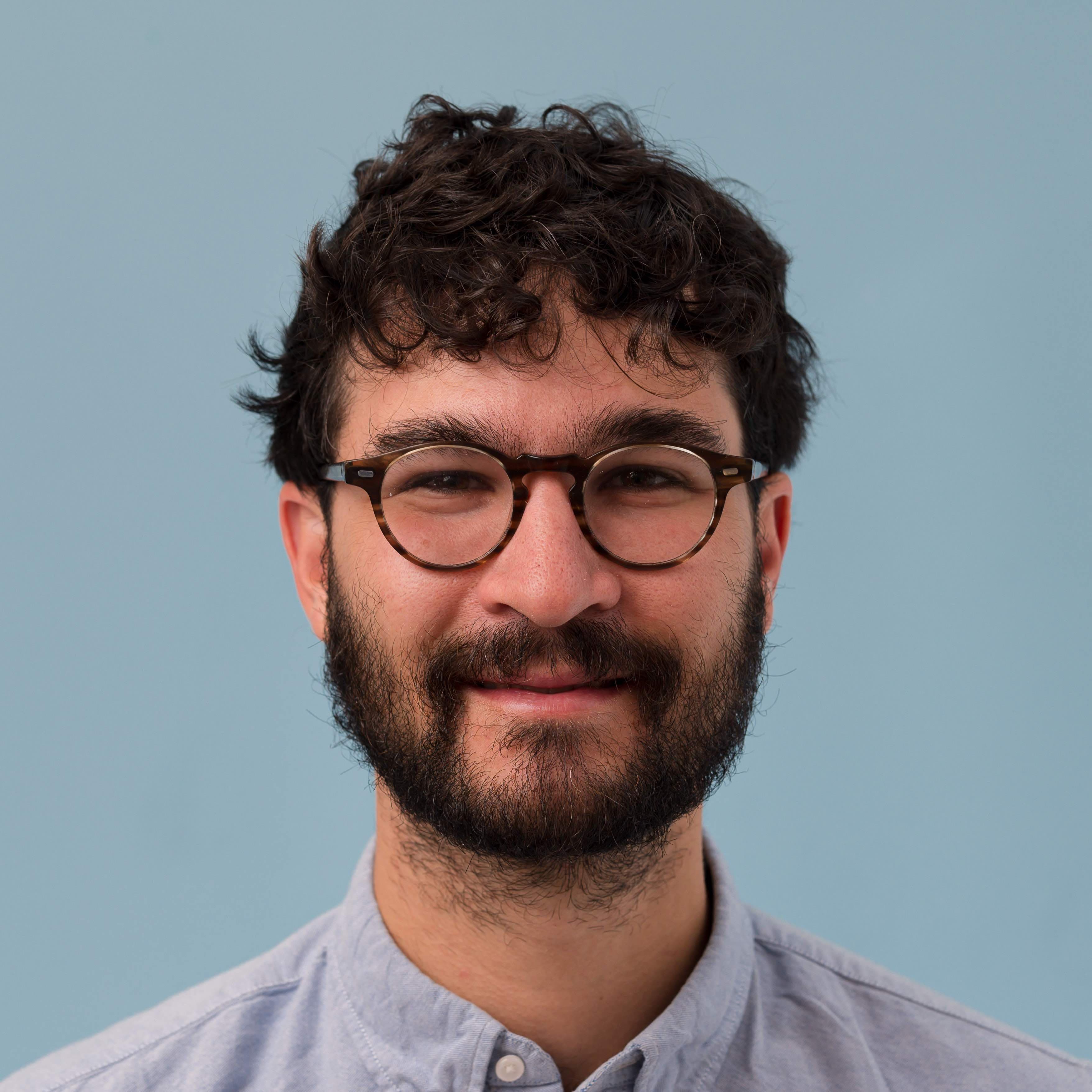 A man with a beard and glasses looks at the camera.