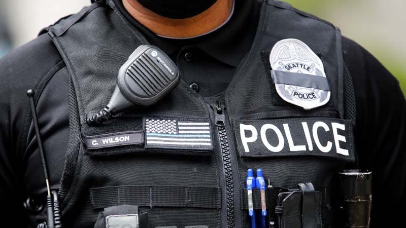 A Seattle police officer wears a "mourning band" for fallen officers over his badge, obscuring the badge number, as Seattle police guard the department headquarters downtown during a rally and march calling for a defunding of Seattle police, in Seattle, W