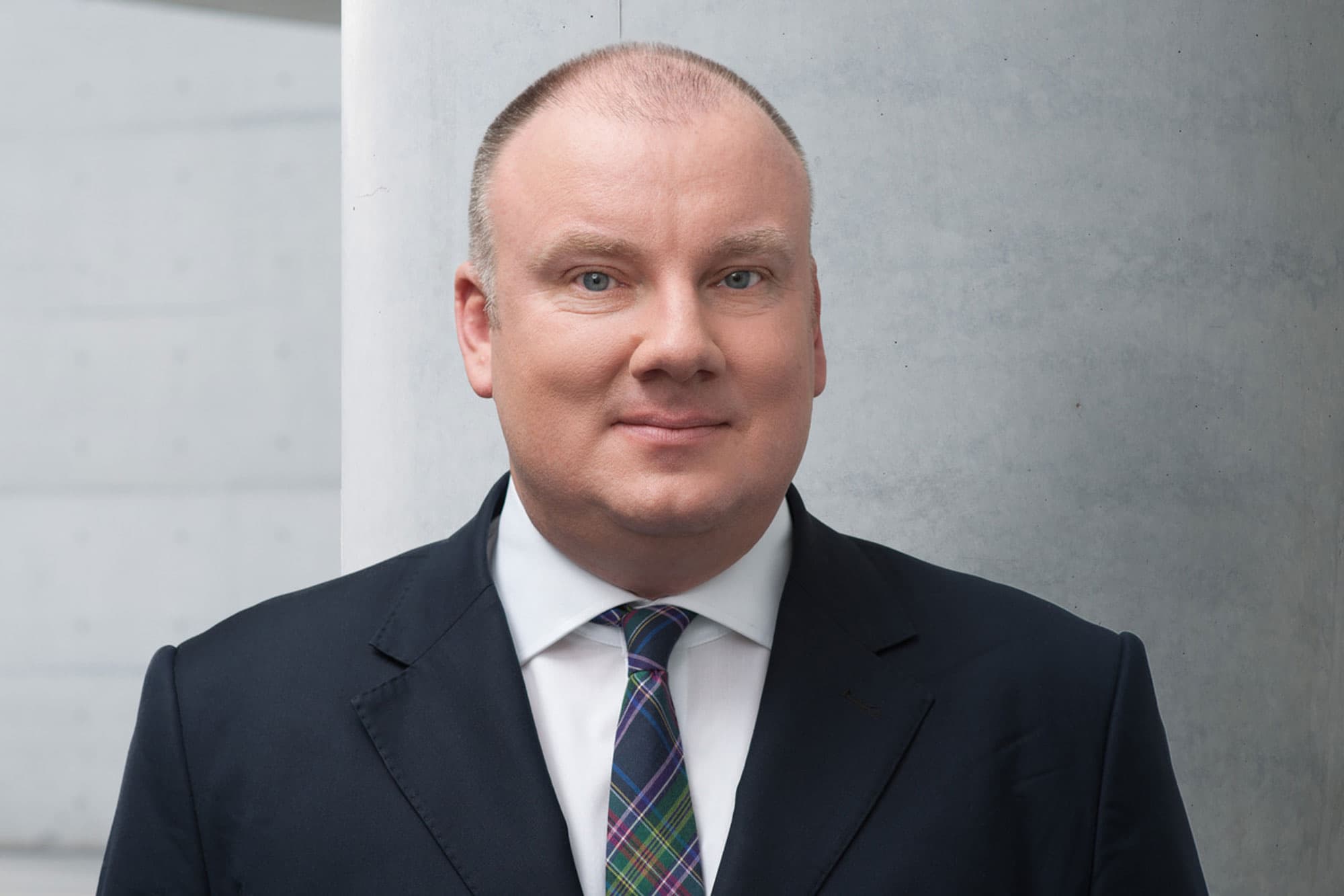 Christian Hochfeld is shown in a portrait photograph wearing a blue suit and plaid tie.