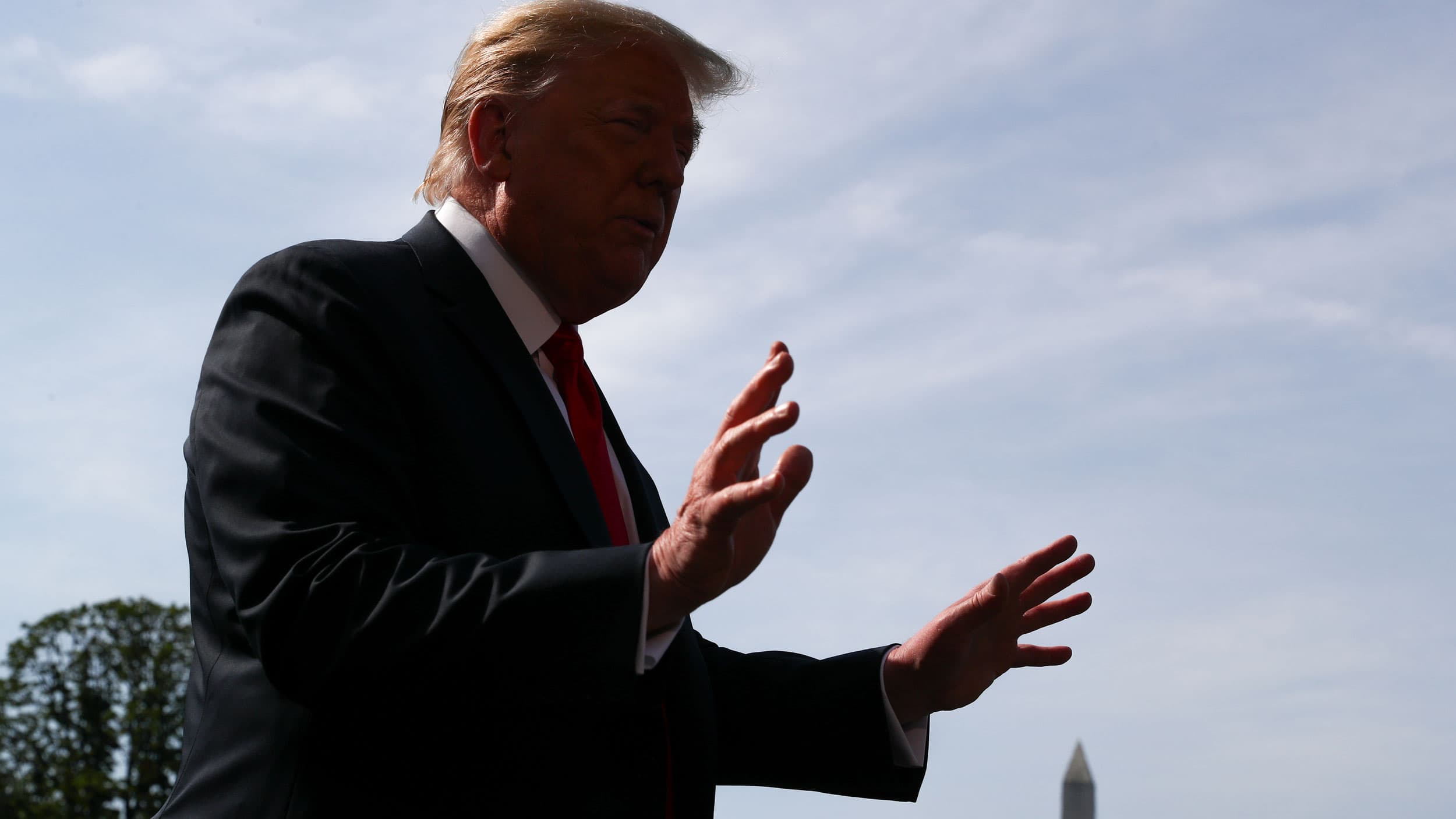 US President Donald Trump is shown in shadow with his hands outstretch and the Washington Monument in the background.