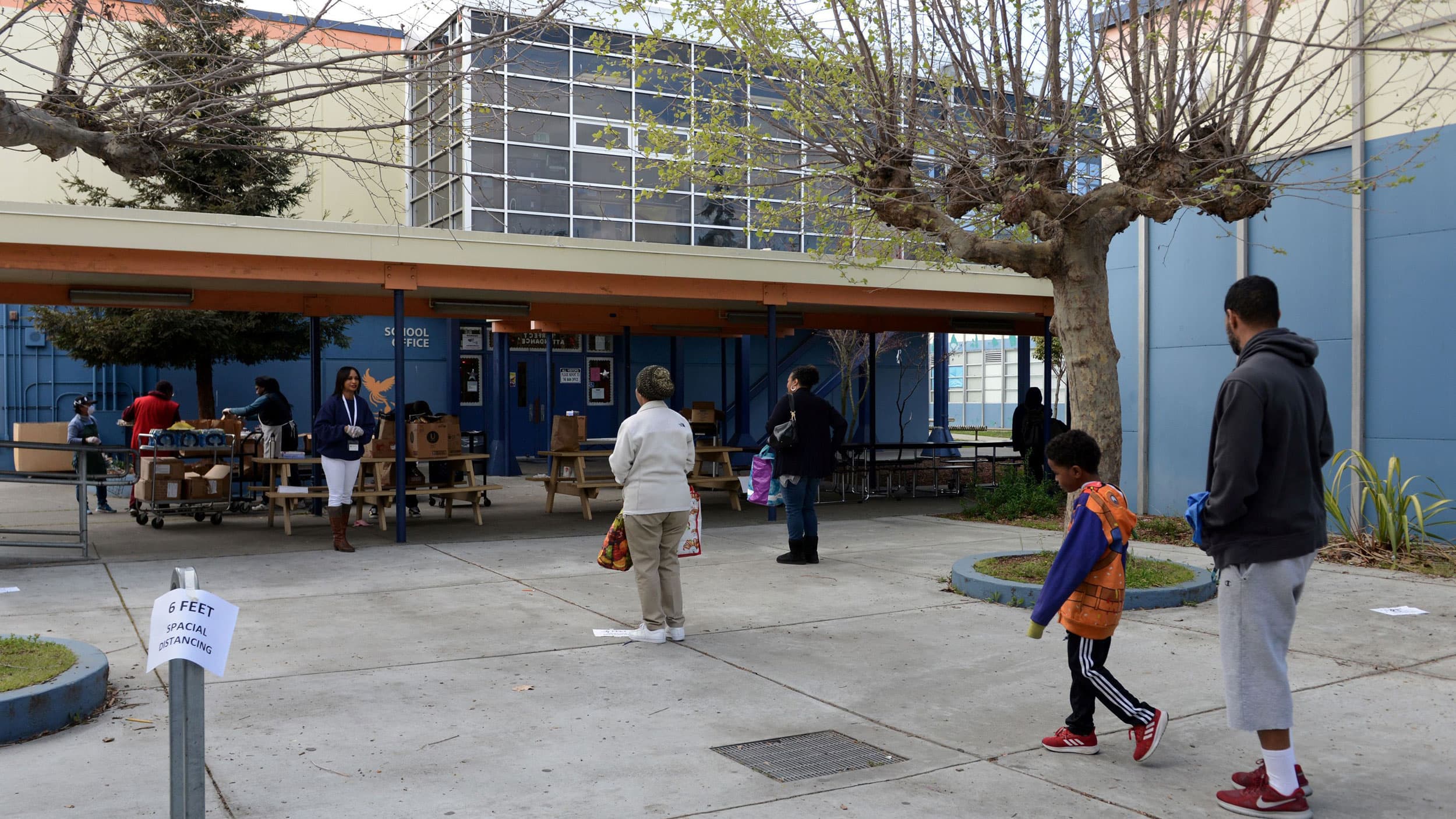 people stand socially distanced in front of a school