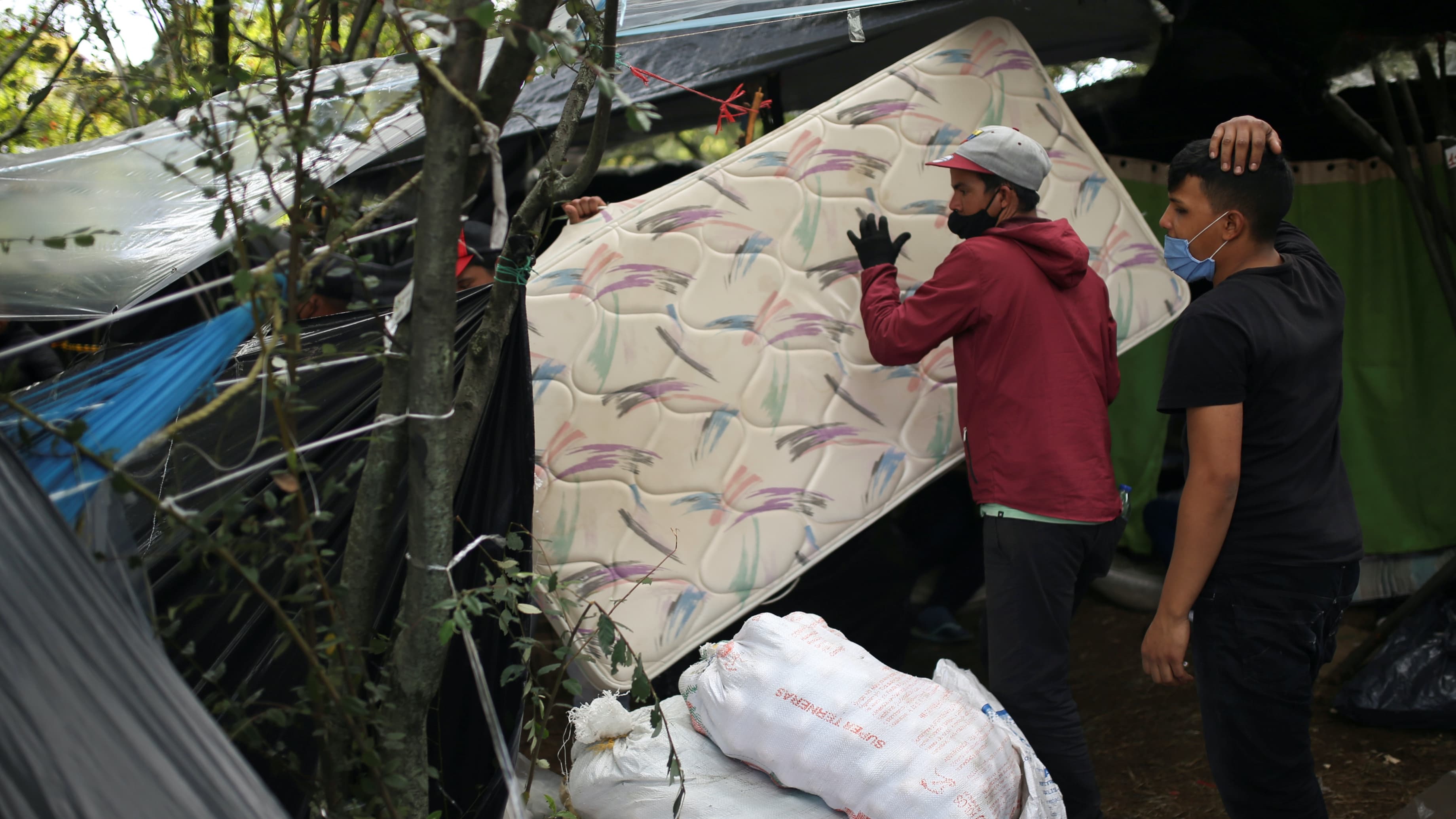 A man wearing a face mask carries a mattress at a makeshift camp
