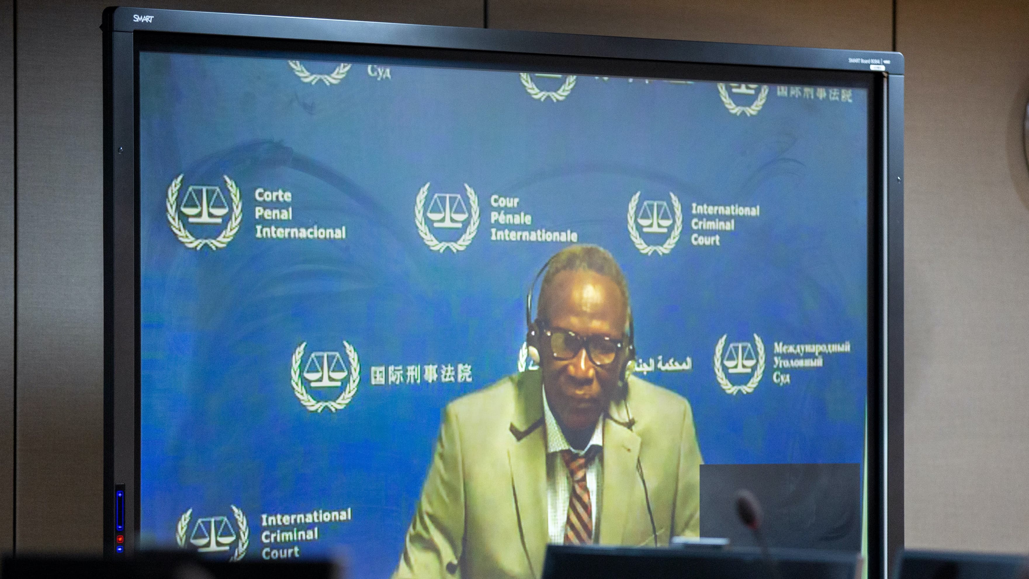 An African man wearing a suit appears on a video screen with a blue background