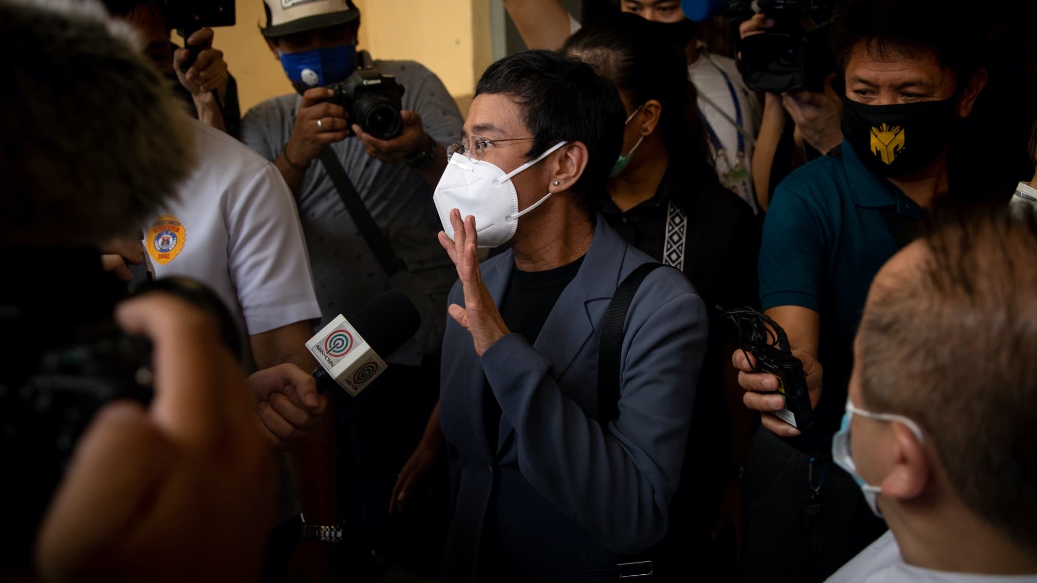 A woman with short hair wearing a face mask and grey suit and waves to cameras