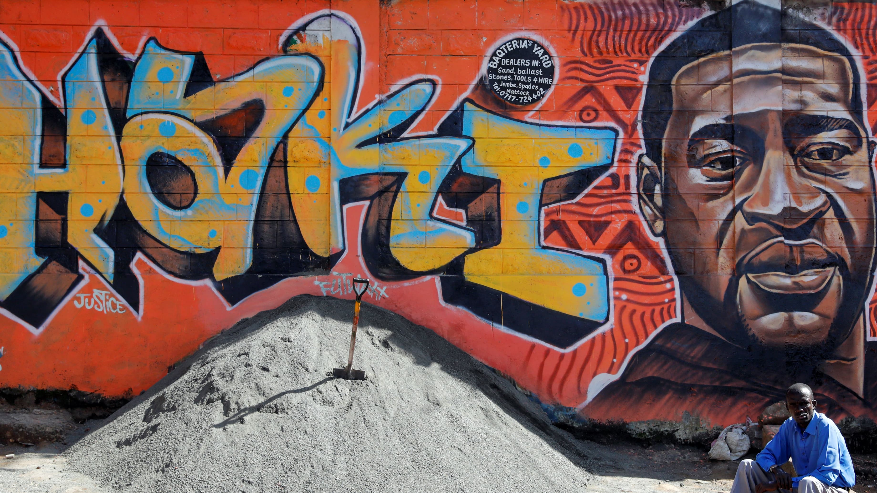 A man sits under a graffiti depicting African American man George Floyd, who was killed by a police officer in Minneapolis, in Kibera, Nairobi, Kenya.
