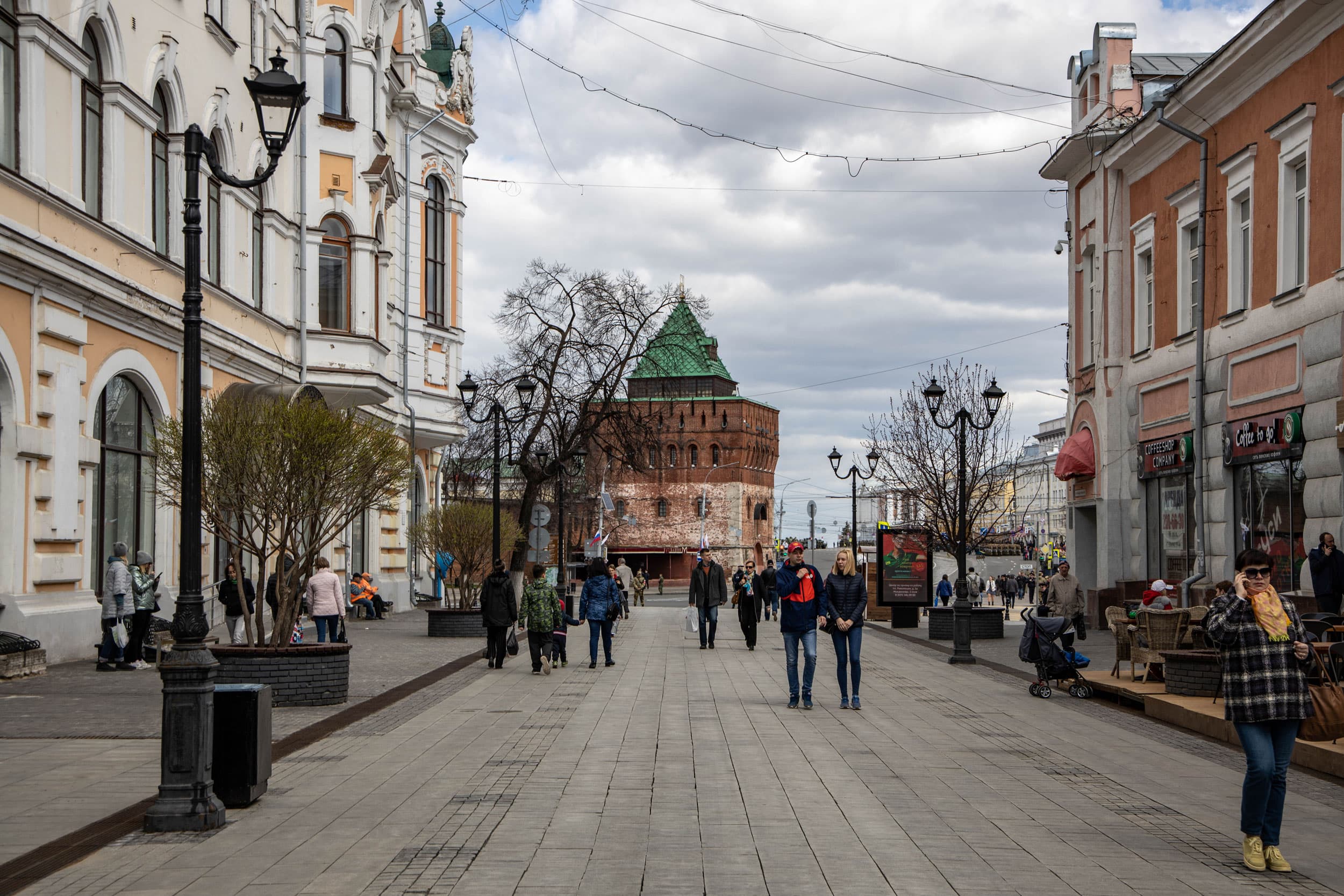 People walk down a street lined with pastel buildings on either side and wrought iron street lamps.