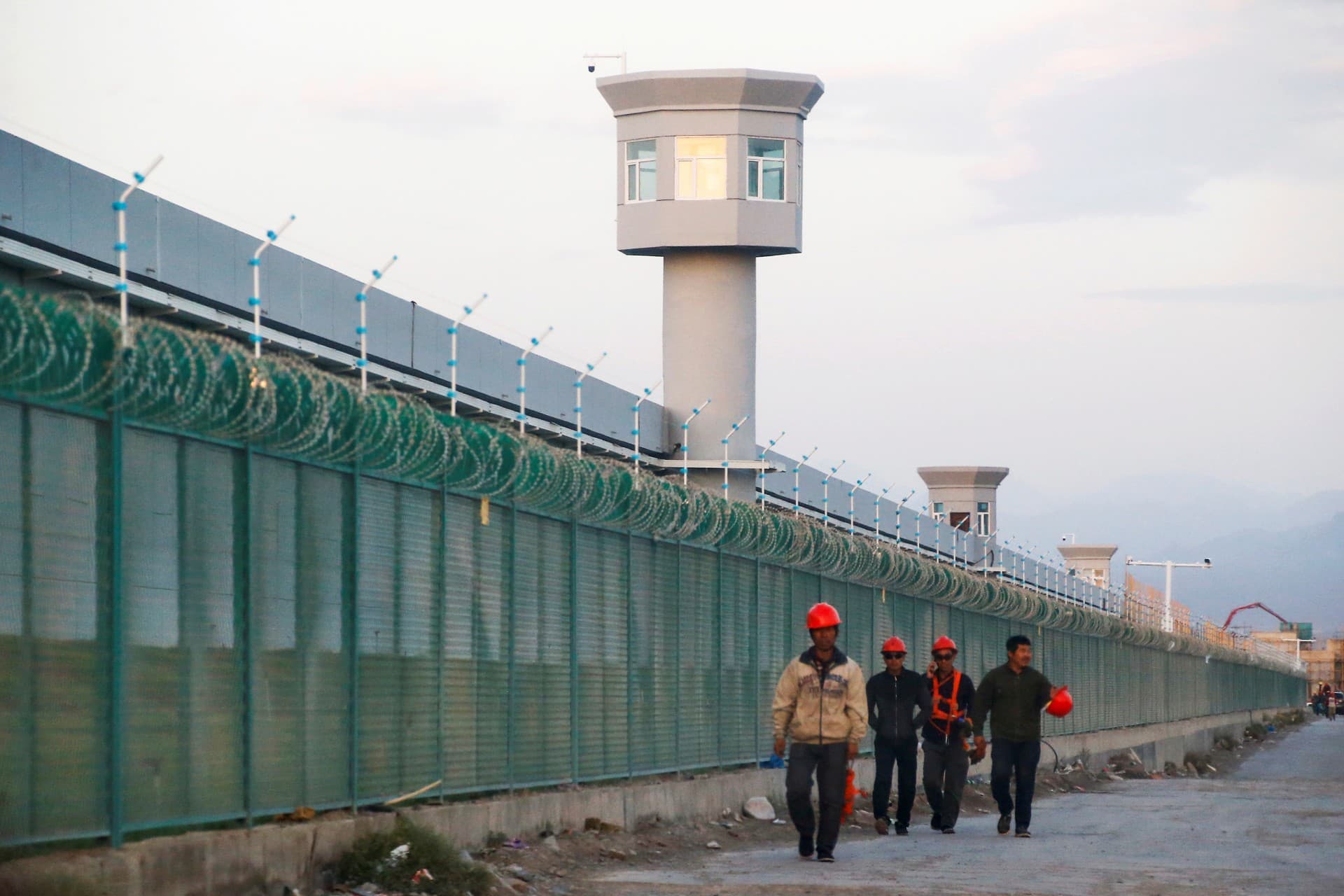 Workers in hard hats and construction vests walking by a fence.
