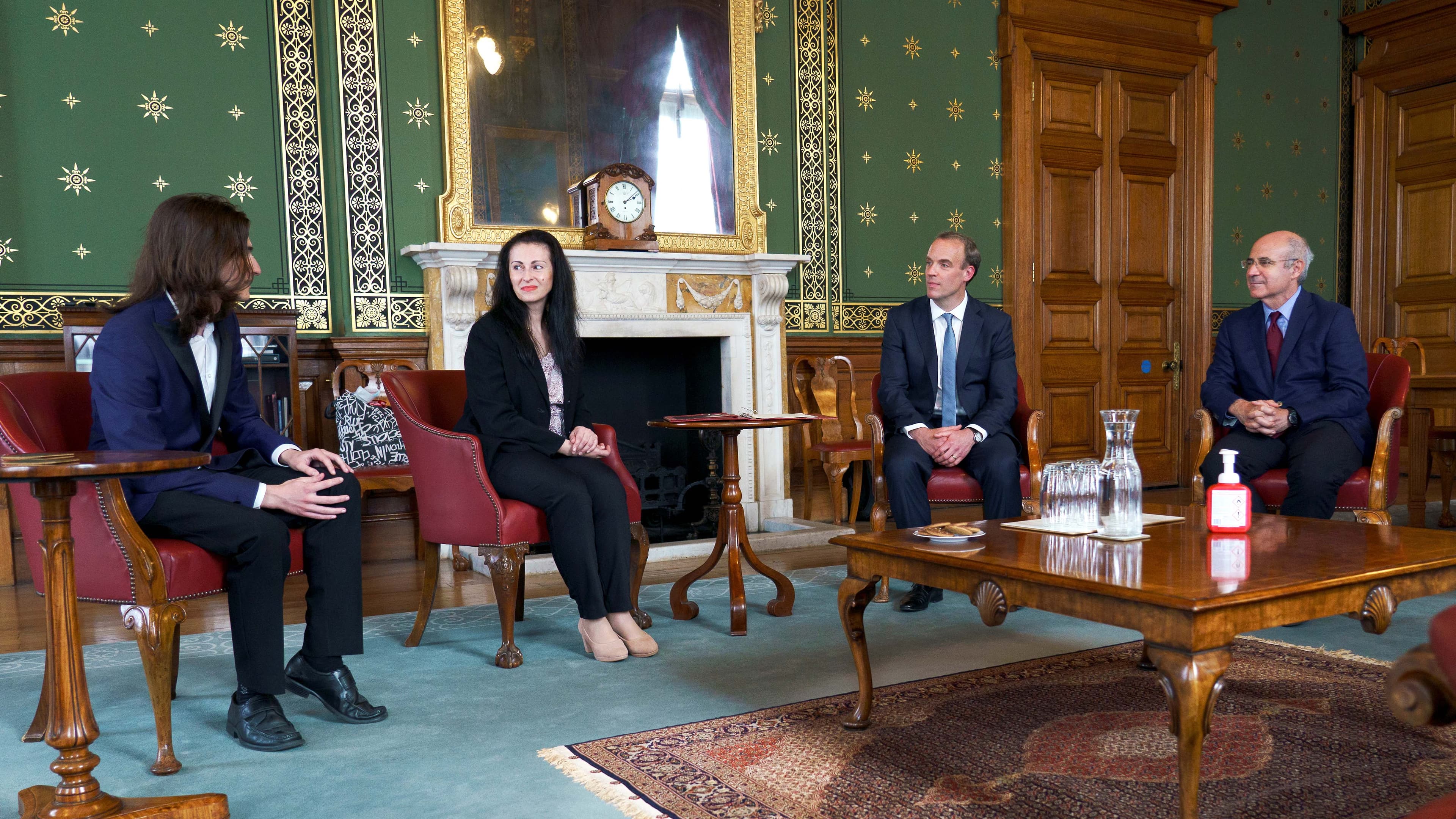A group of four people sit in red chairs in an elegant room with green and gold-starred walls
