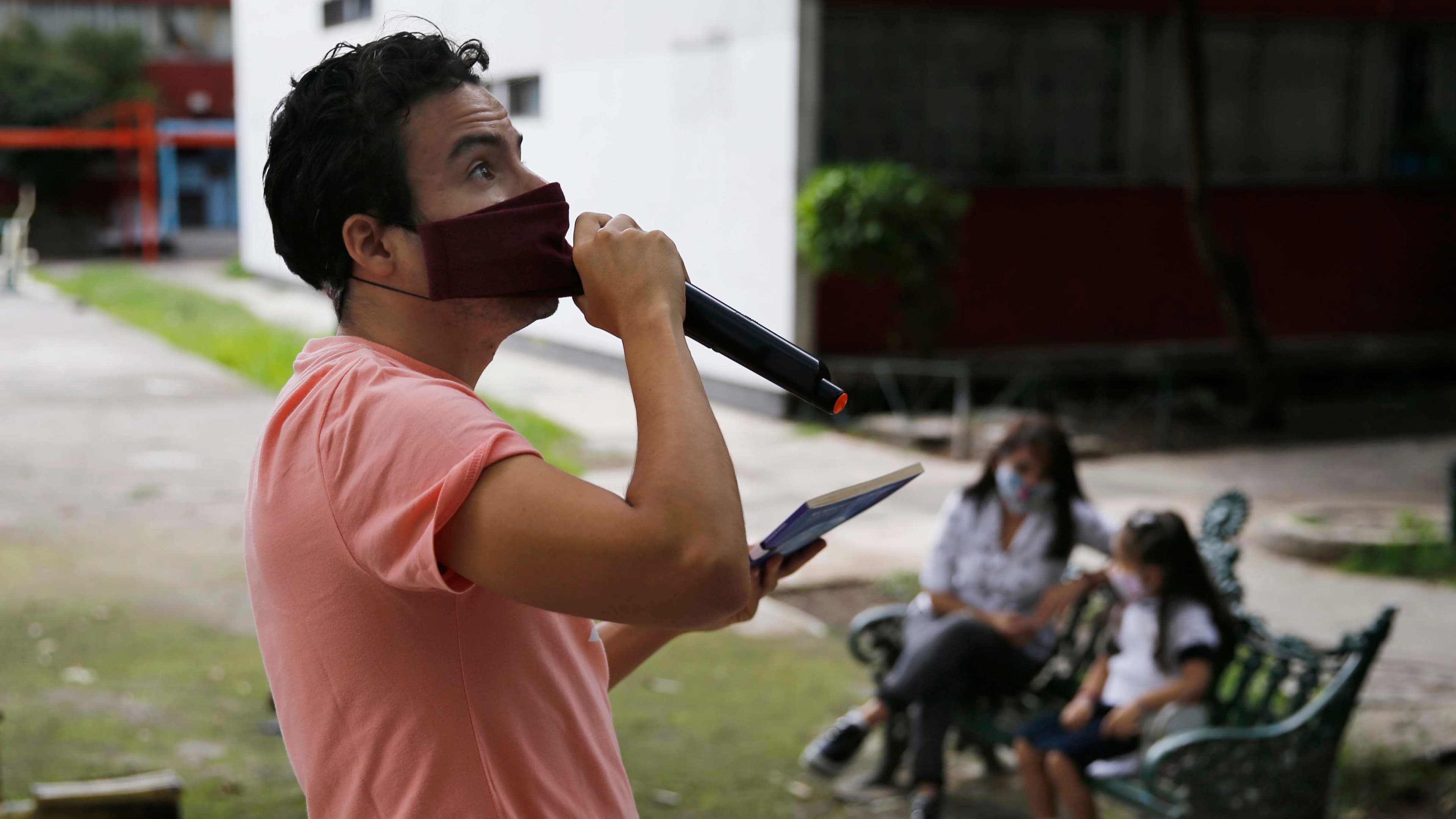 Residents listen from a bench, background, as Percibald García reads children's books aloud outside the high-rise buildings in the Tlatelolco housing complex, in Mexico City, on July 18, 2020.