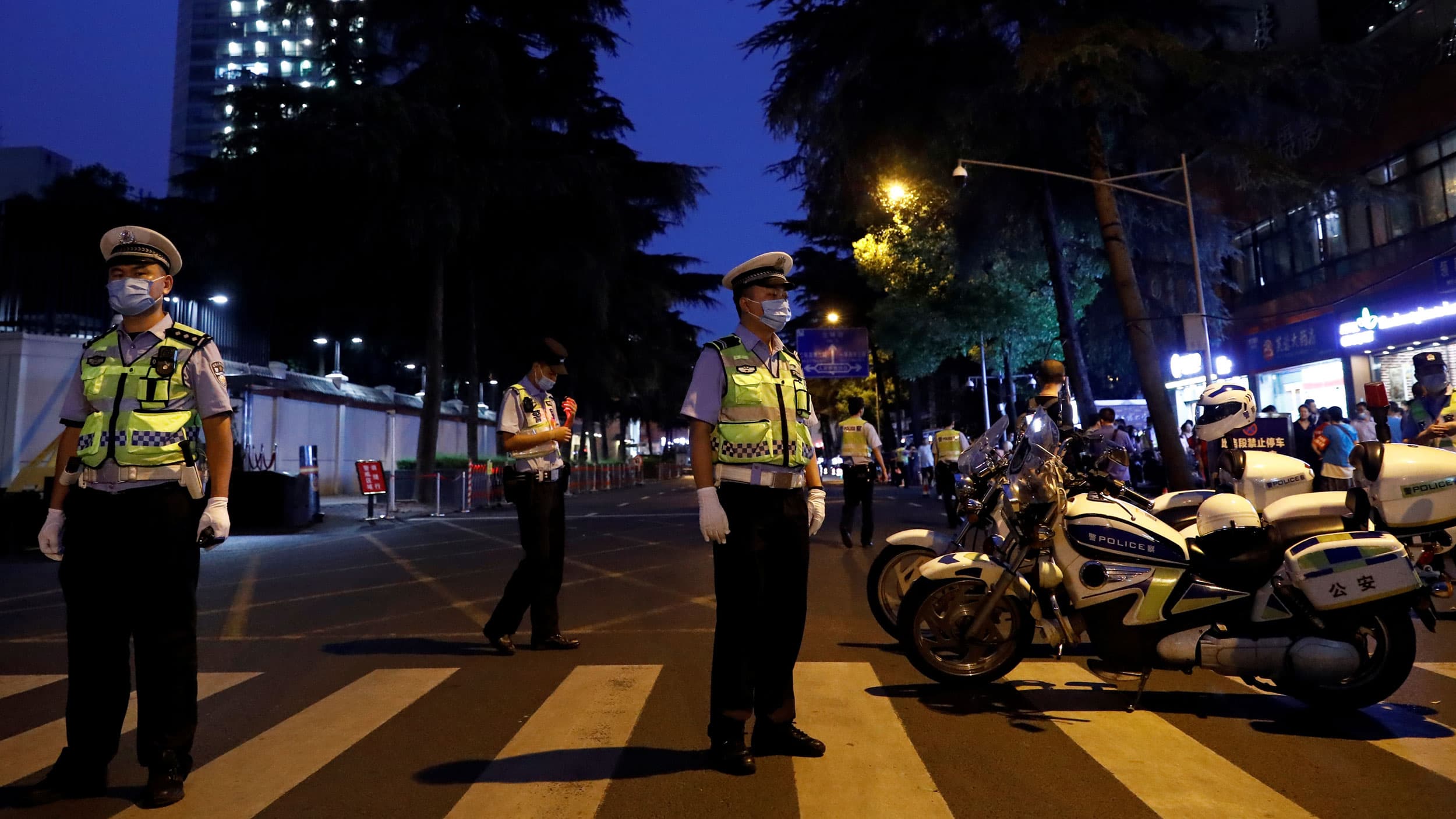 Several security personnel are shown standing in the street and wearing reflective vests next to police motorcycles.