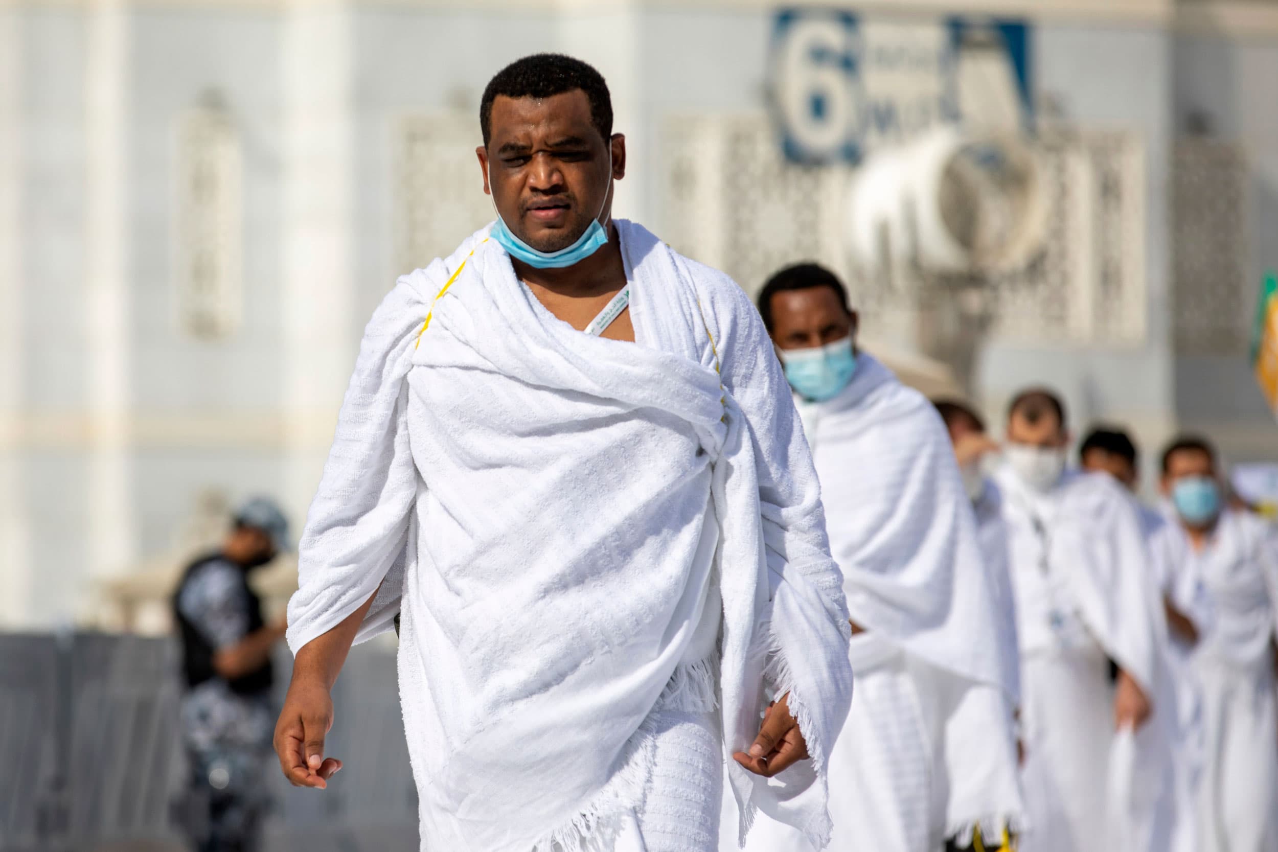 A close-up photograph shows a man wearing a white robe and a face mask hung below his chin.
