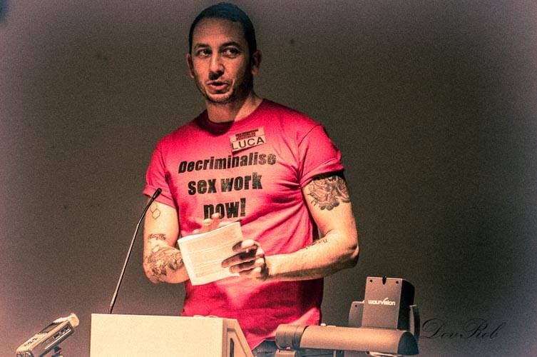 A man wears a red shirt with a message to decriminalize sex work.