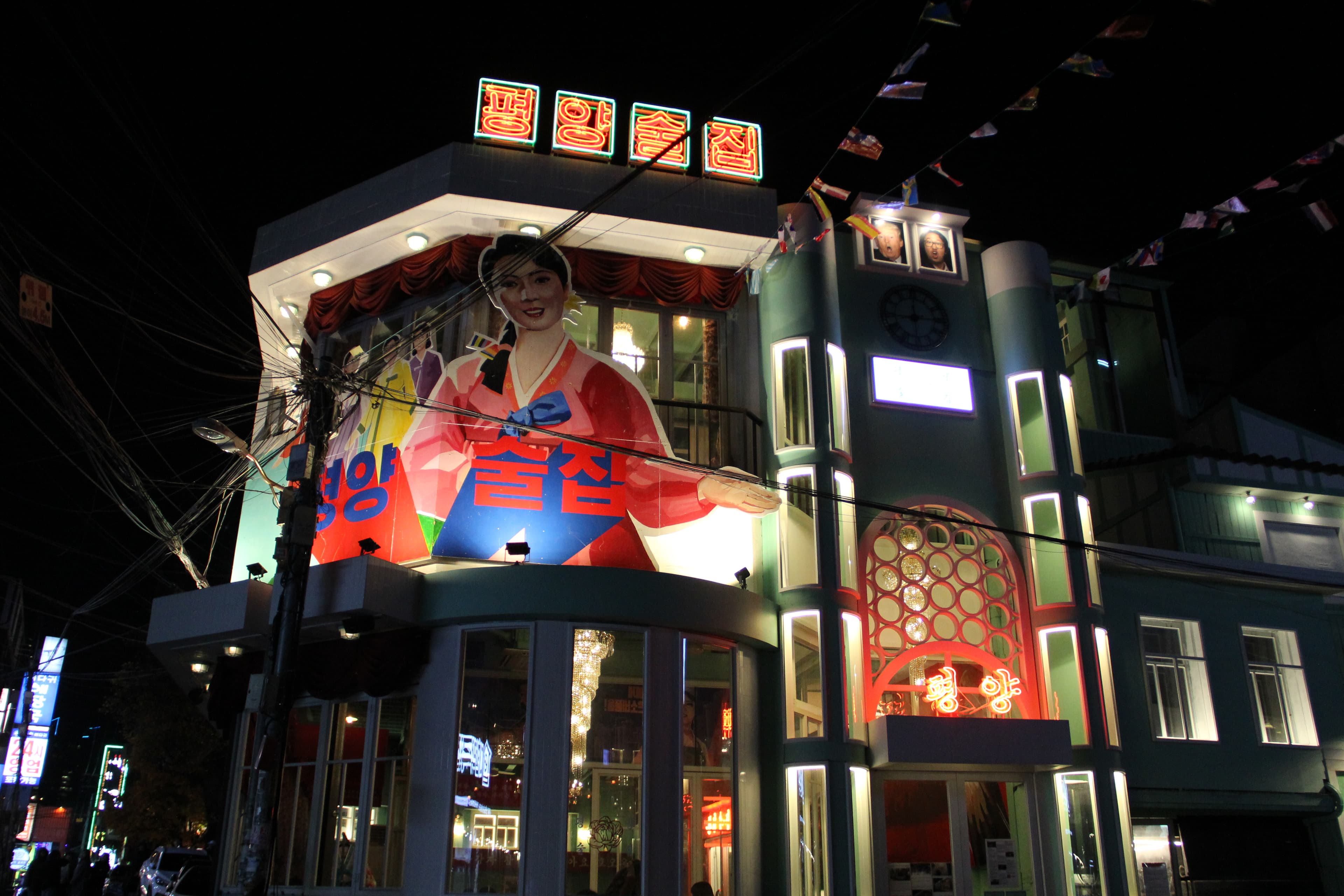 The outside of Pyongyang Pub features a drawing of a smiling North Korean woman. Jolly North Korean tunes blast from the speakers at the entrance