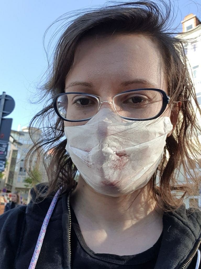 A woman with glasses wears a sweatshirt and a white face mask.