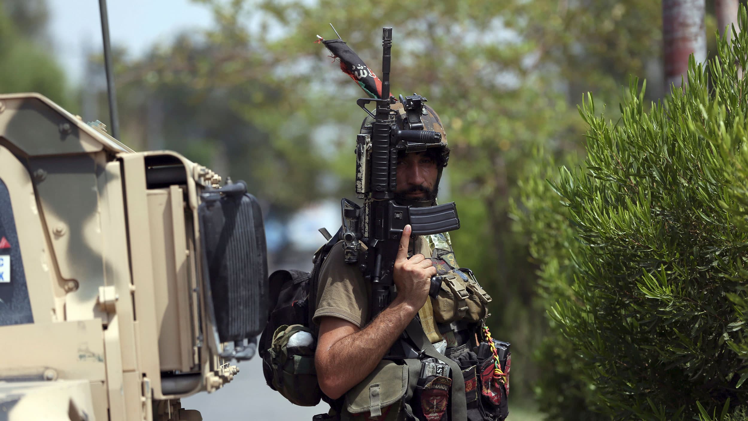 An Afghan security person is shown holding a large rifle pointed up and wear a helmut and other military-grade equipment.