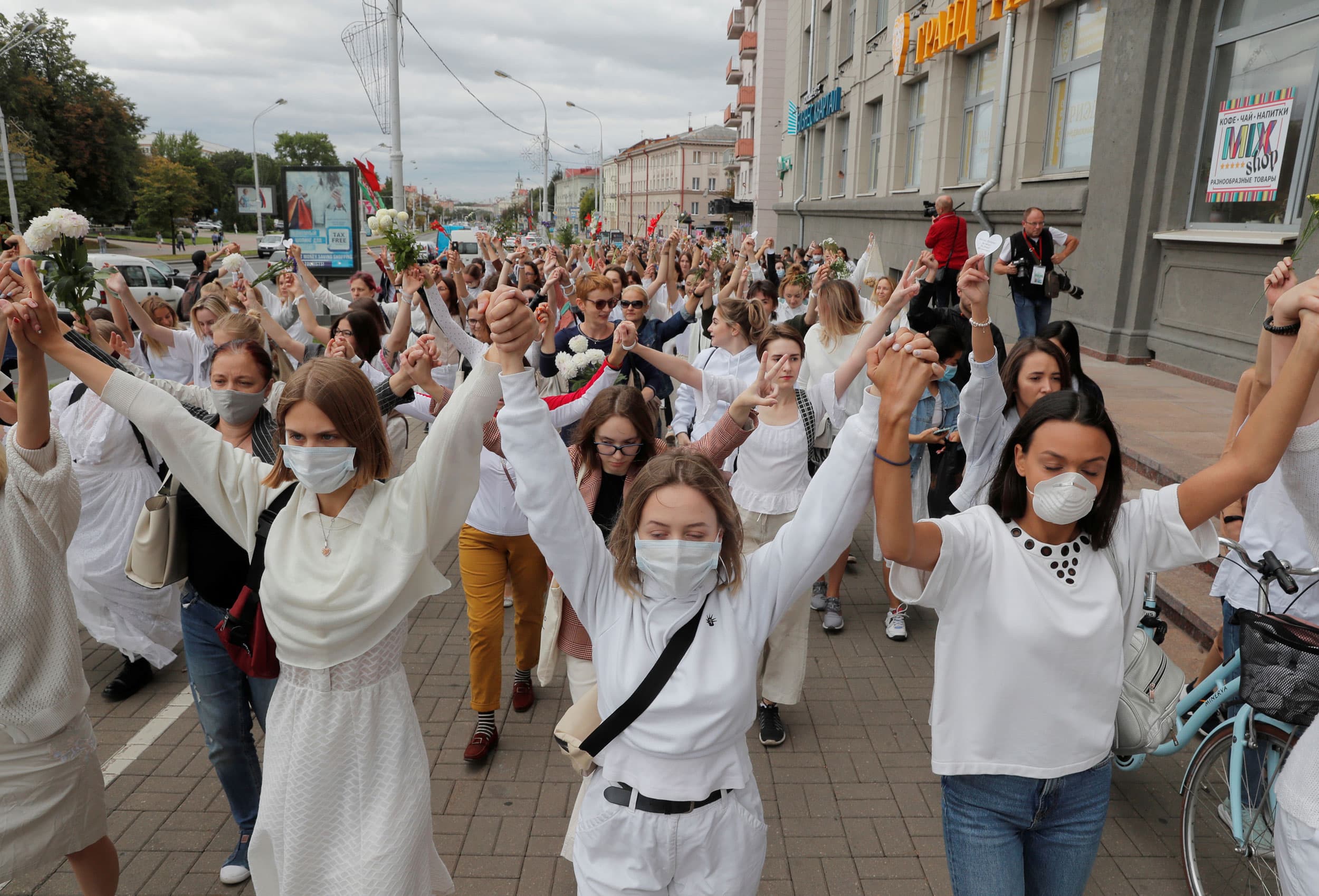 A large crowd of women are shown wearing white and holding their hands in the air.