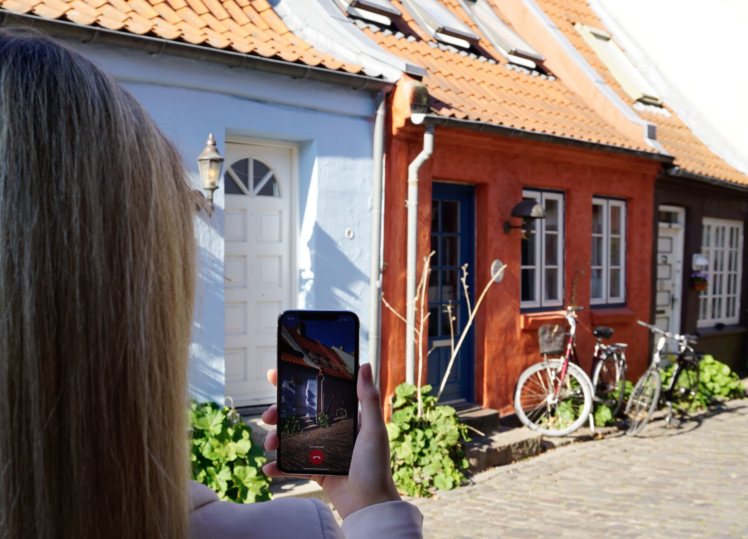 A woman uses Be My Eyes video chat app to connect with a sighted volunteer to show a house on a cobblestone street.