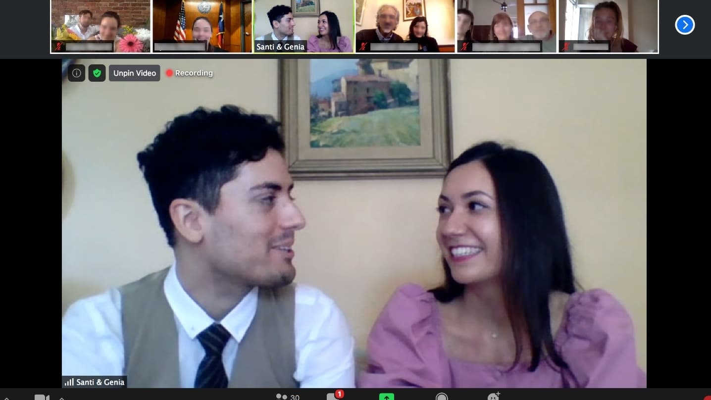 A man in a suit and woman wearing a pink dress look at each other on a screen with smaller boxes of peoples' faces above them