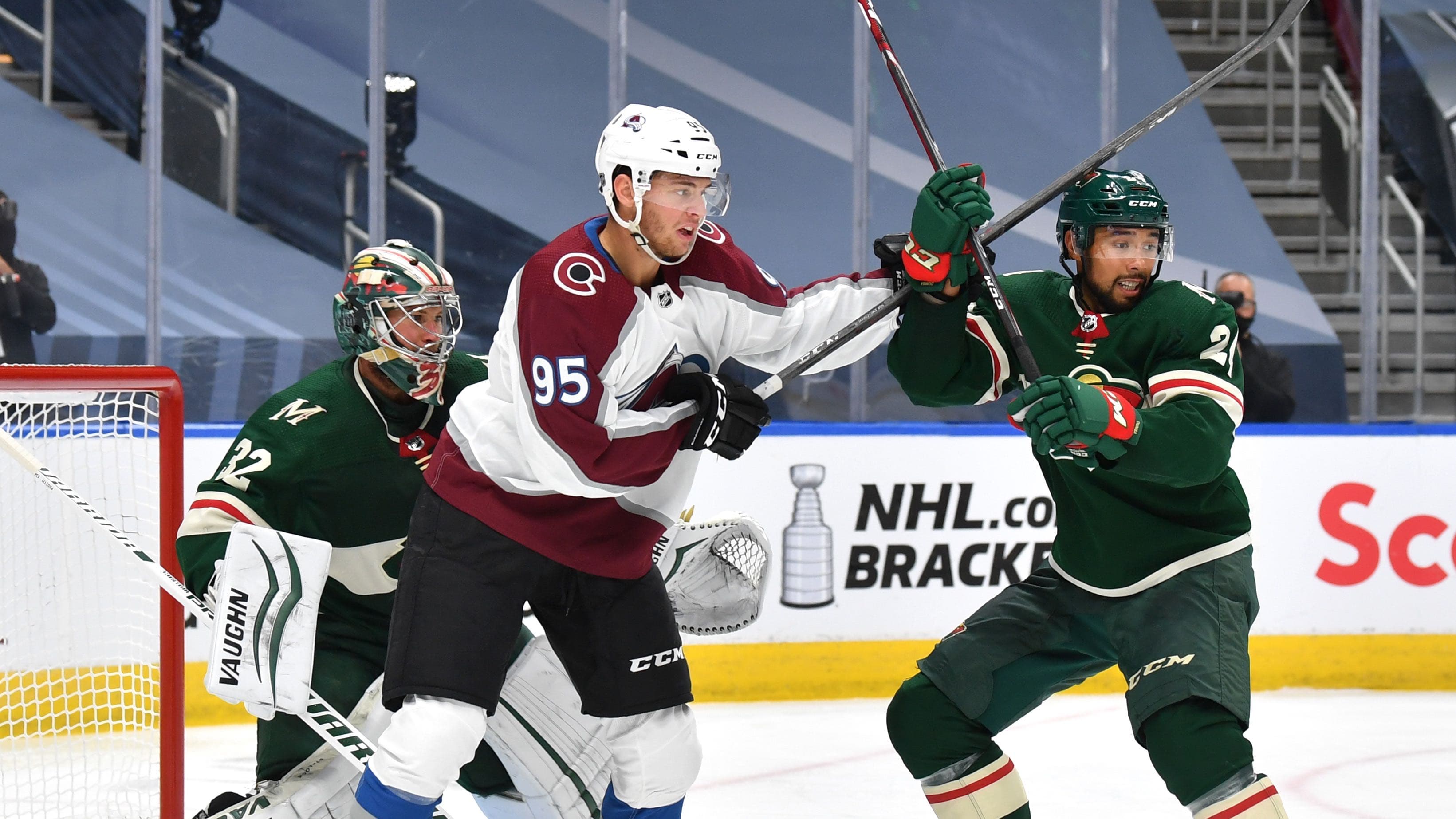 Men wearing hockey gear play hockey on the ice in a stadium.
