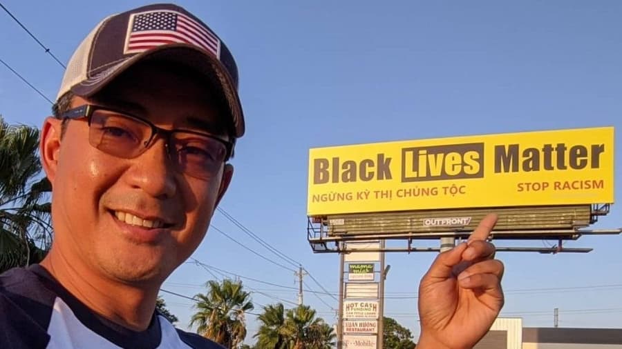 A man points his finger at a yellow billboard with black writing in Vietnamese and English