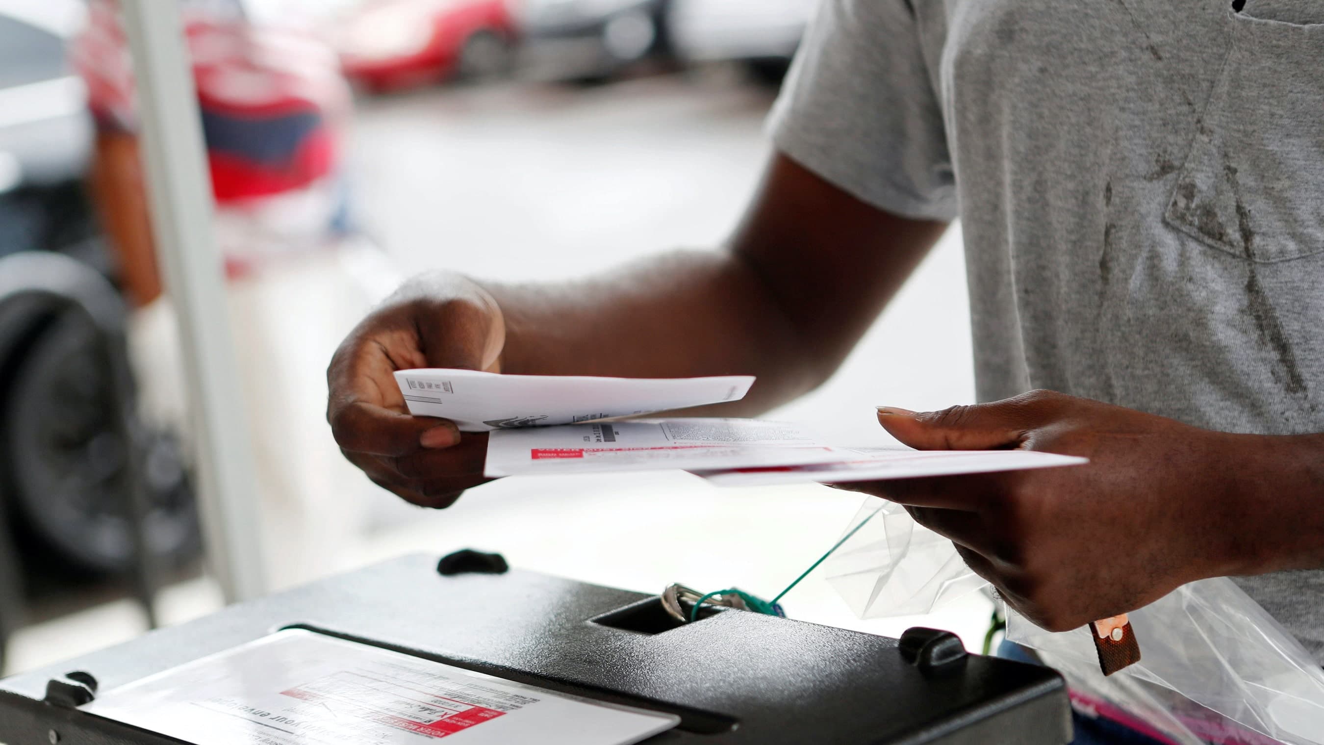 A person wearing a gray shirt holds two paper ballots and places them in a box.