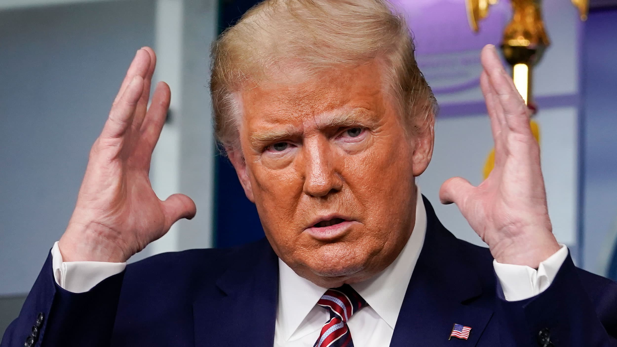 US President Donald Trump his shown with his hands raised near his face and wearing a dark suit and stripped tie.