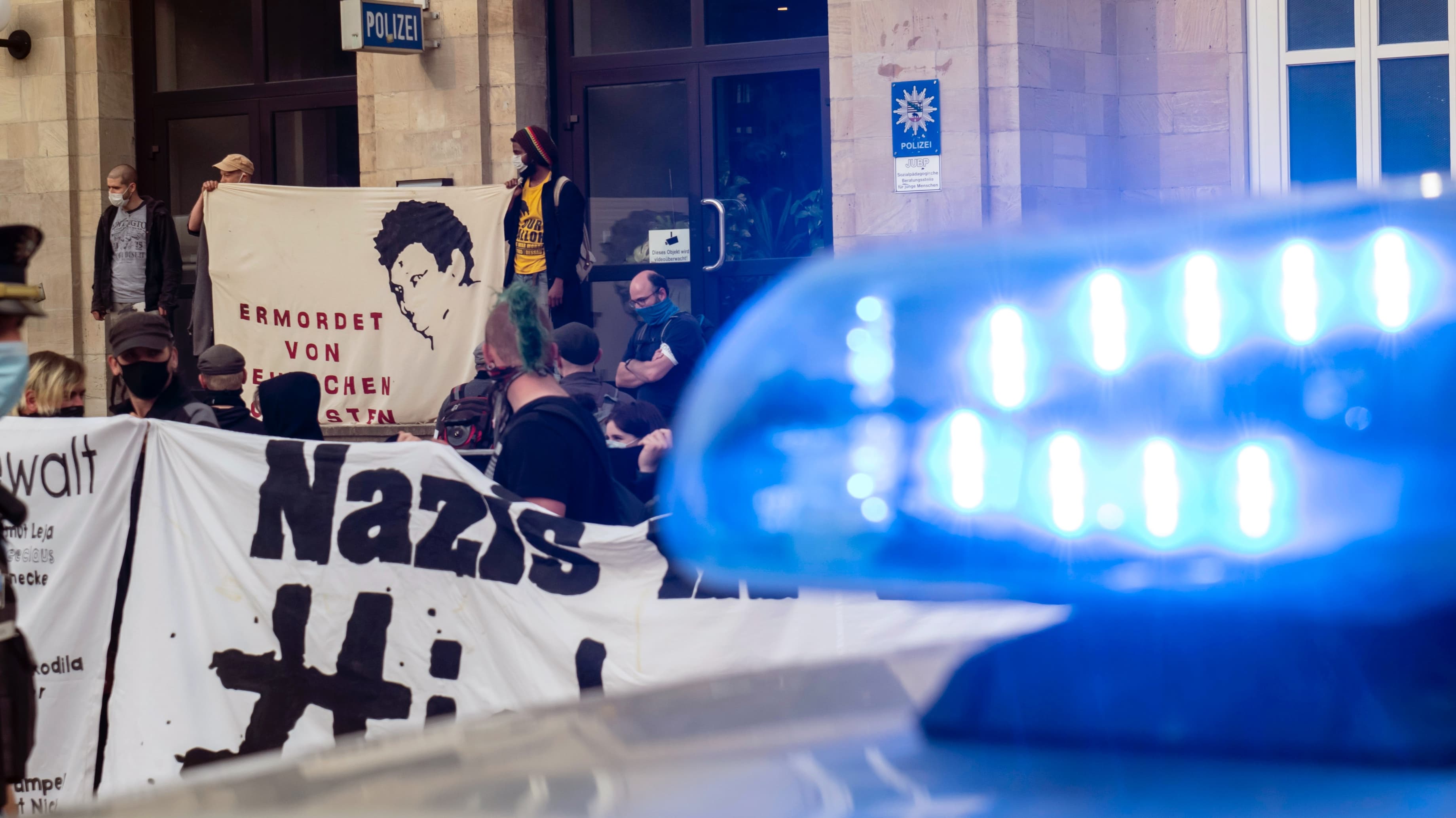 A sign with the written word nazi in black appears near the blue lights of a police vehicle