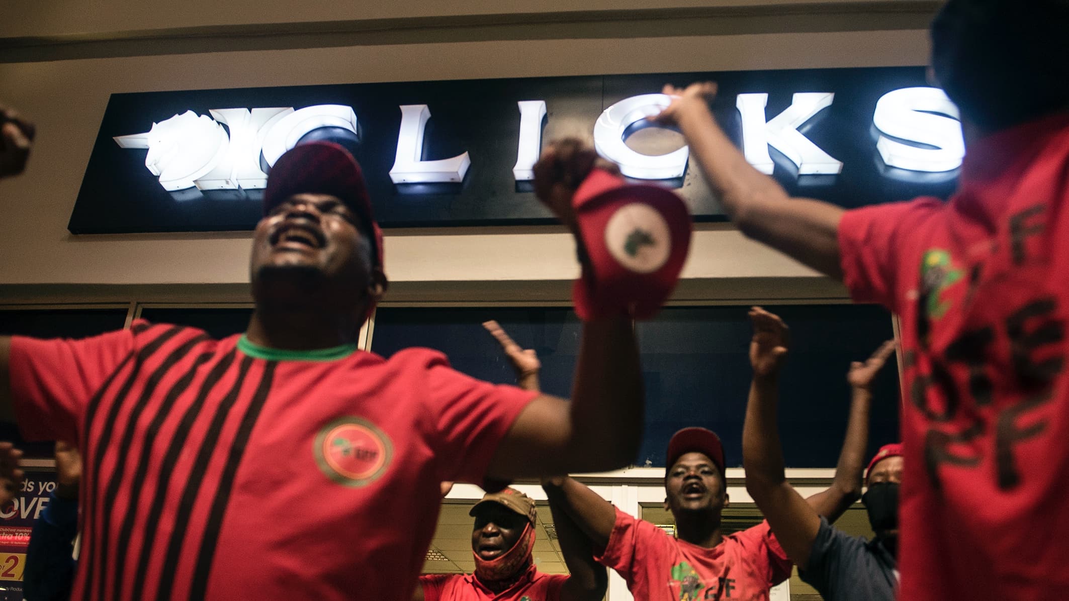 Men and women wearing red political shirts chant in front of a department store in South Africa