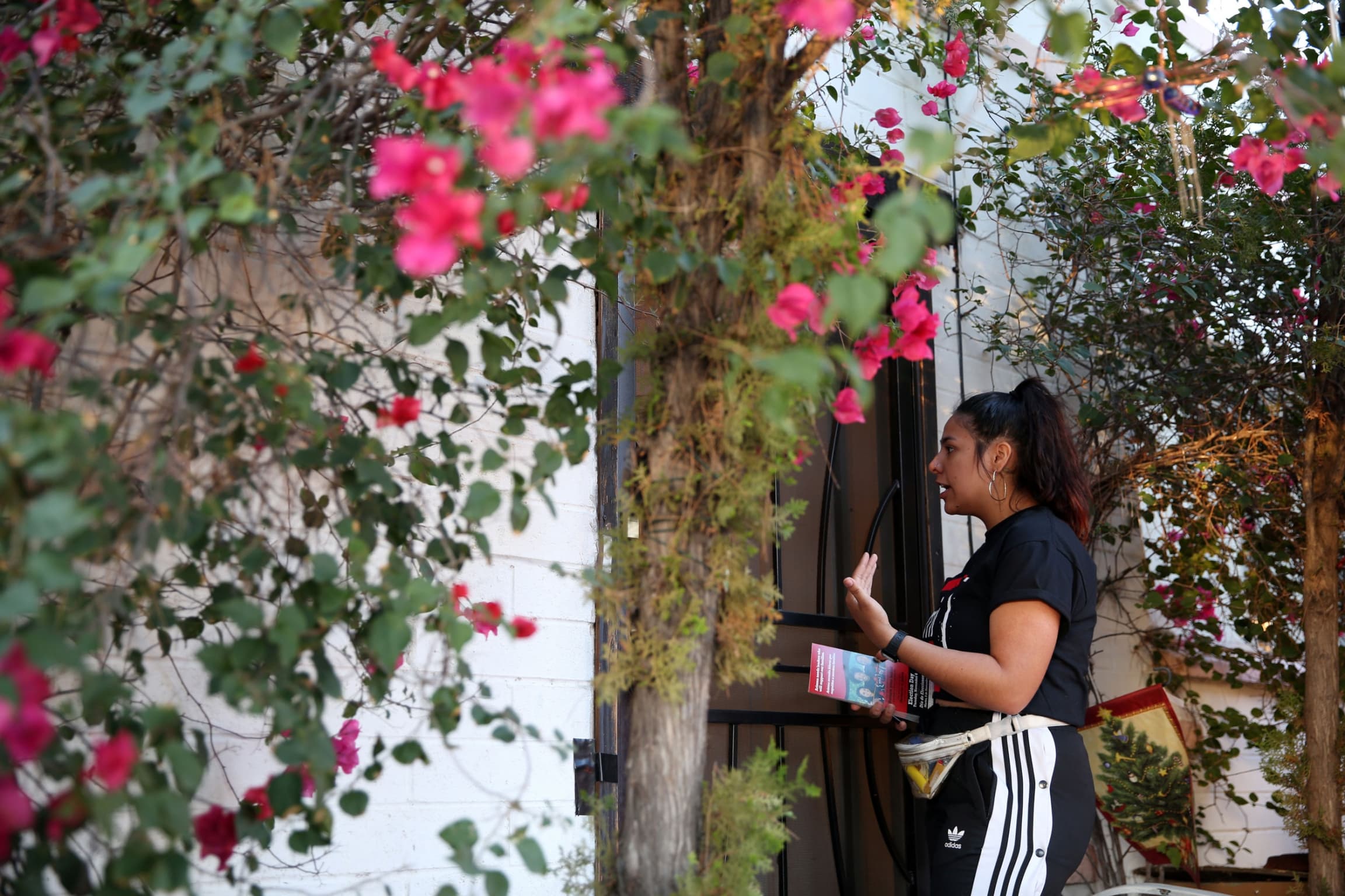 Una mujer habla con una persona que esta dentro de una casa rodeada por un jardin.