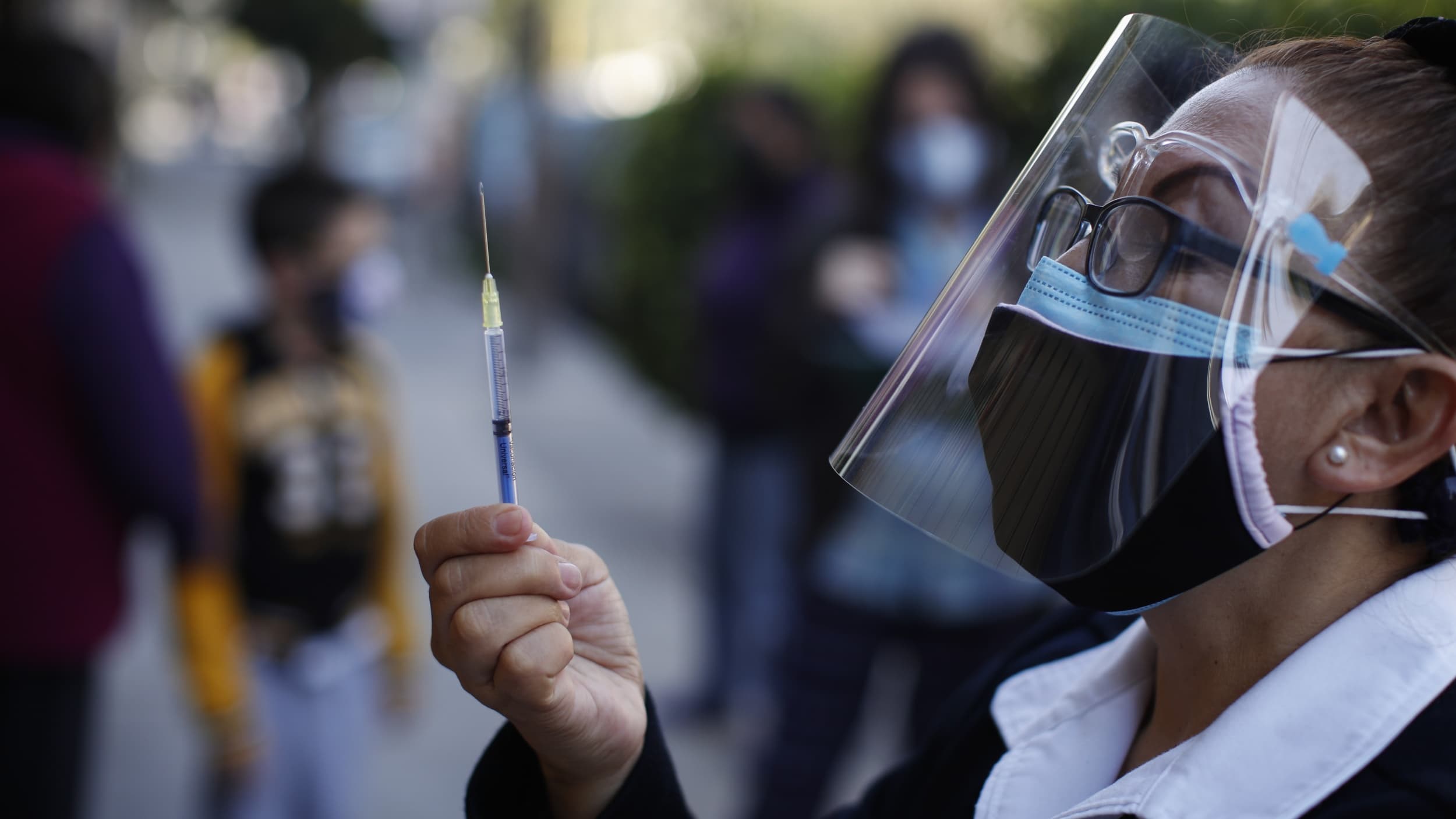 Woman in PPE holds up a vaccine