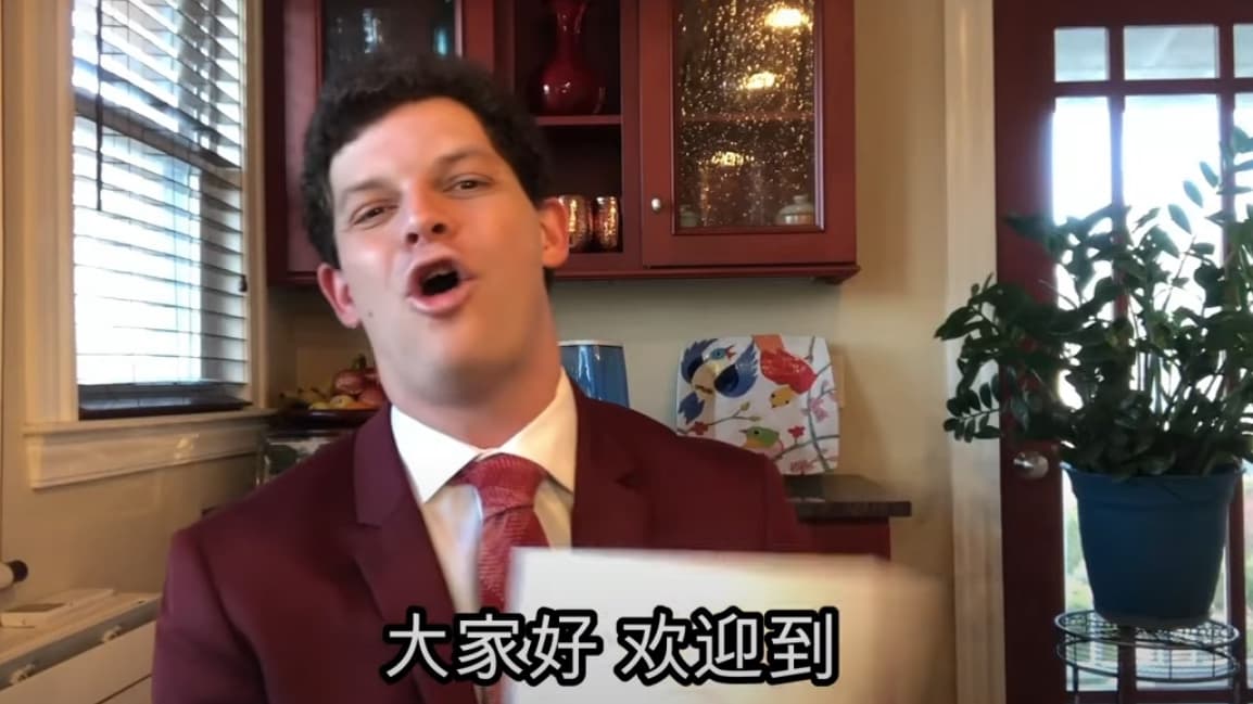 A white man wearing a suit talks in a kitchen with Chinese lettering at the bottom of the screenshot.
