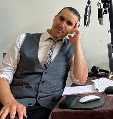 Portrait of a man wearing a suit sitting at a table with a microphone.