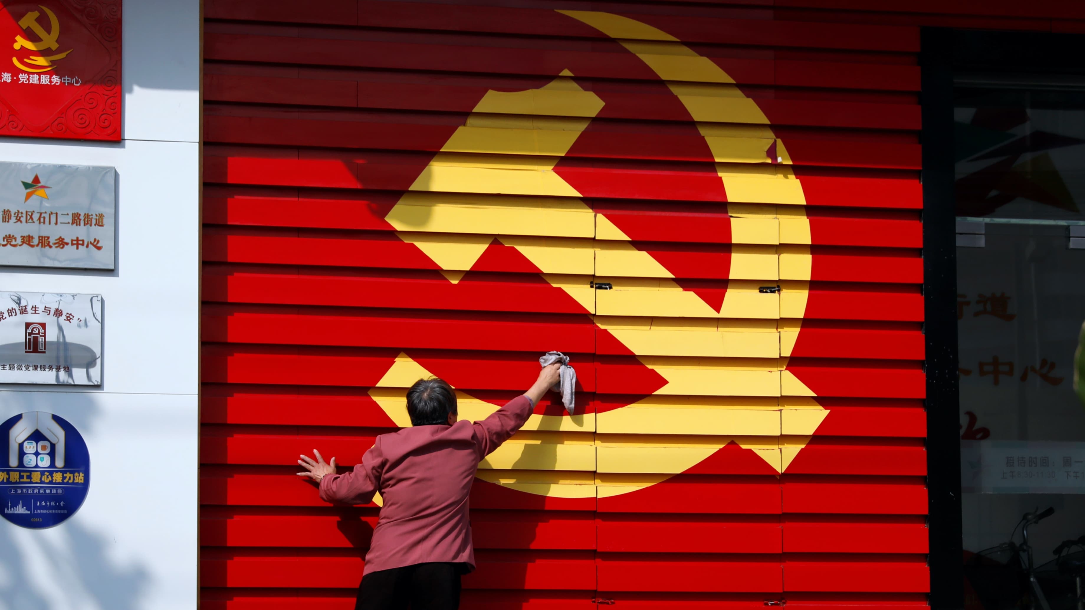 A person washes a wall with painted big yellow hammer and sickle of the Chinese Communist Party.