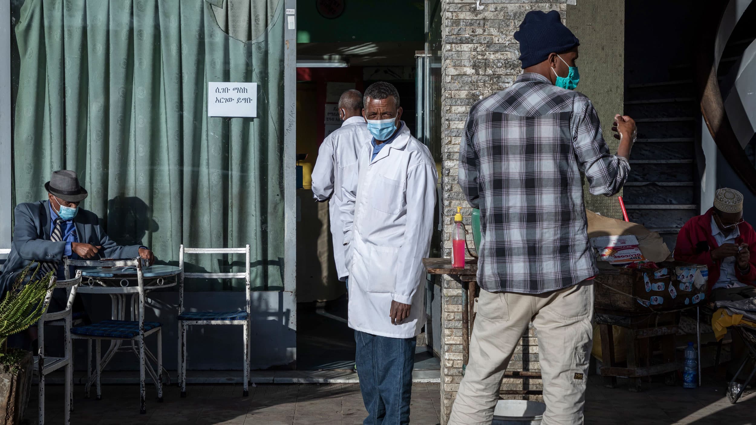 Several people are shown standing and sitting at a tea room with several wearing face masks.