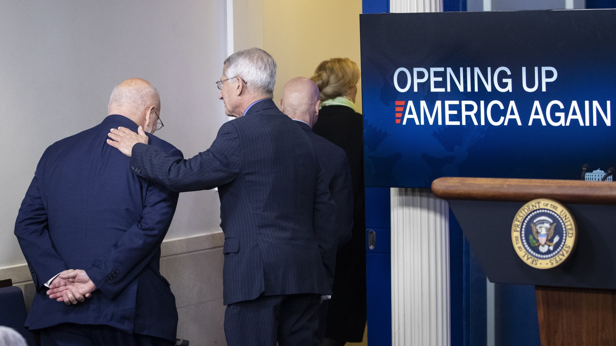 CDC Director Dr. Redfield and Dr. Fauci leave a meeting together. A screen displays the text, "Opening Up America Again."