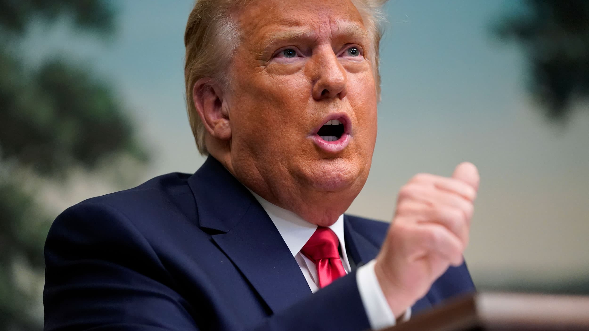 US President Donald Trump speaks with his right hand raised.