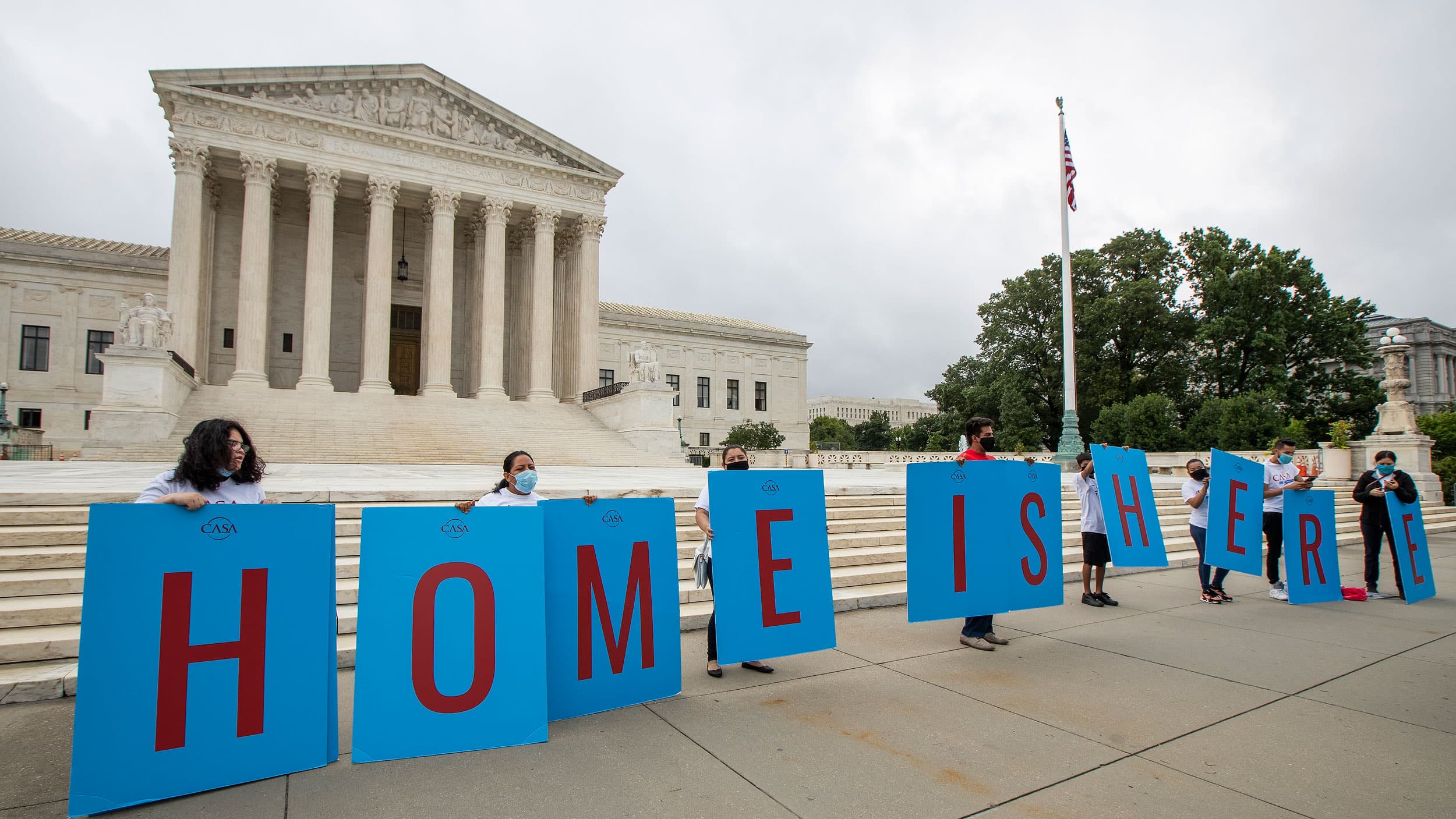 Several people are shown standing behind large placards that together spell out, 