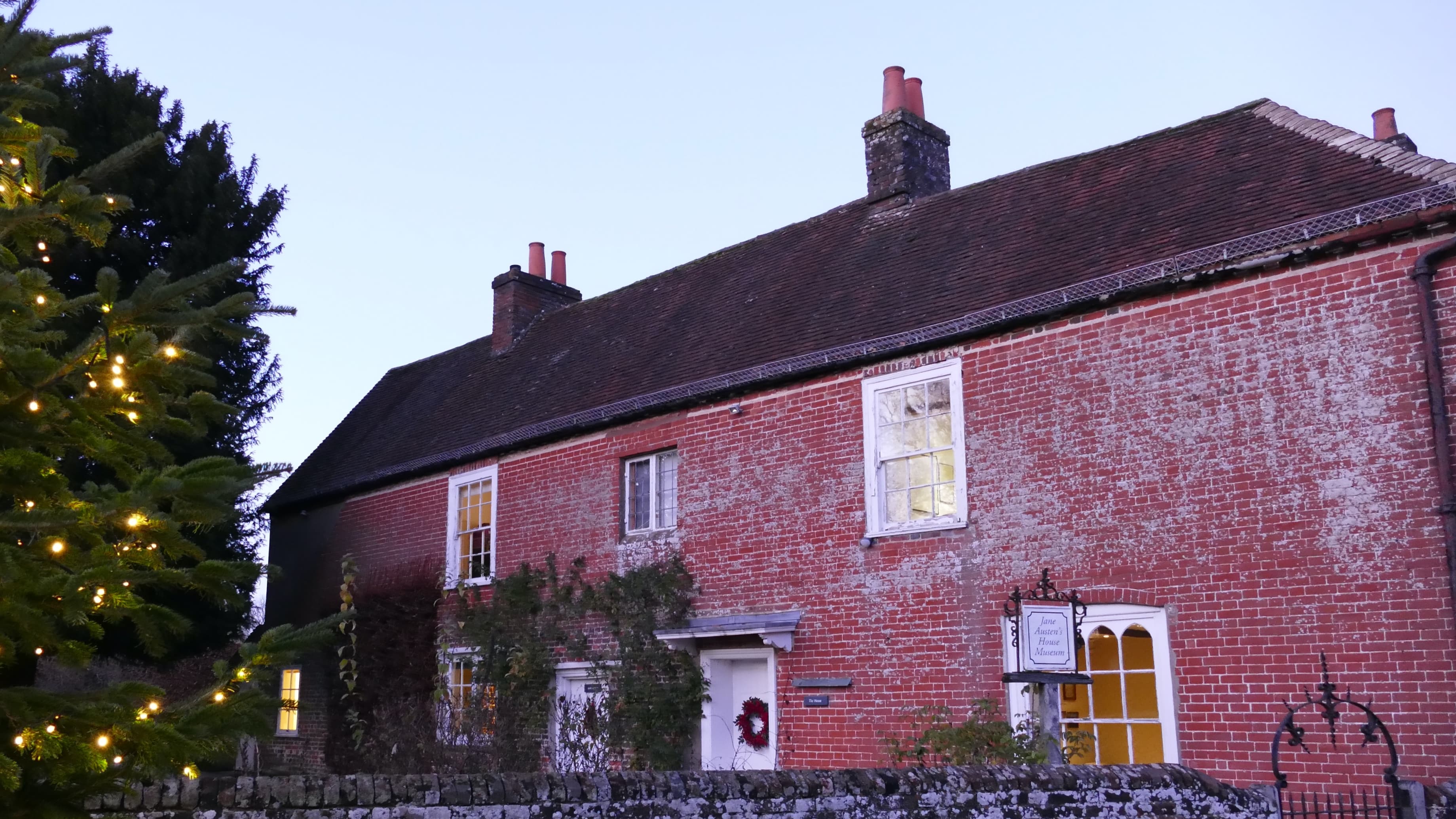 A red brick house next to a tree with Christmas lights