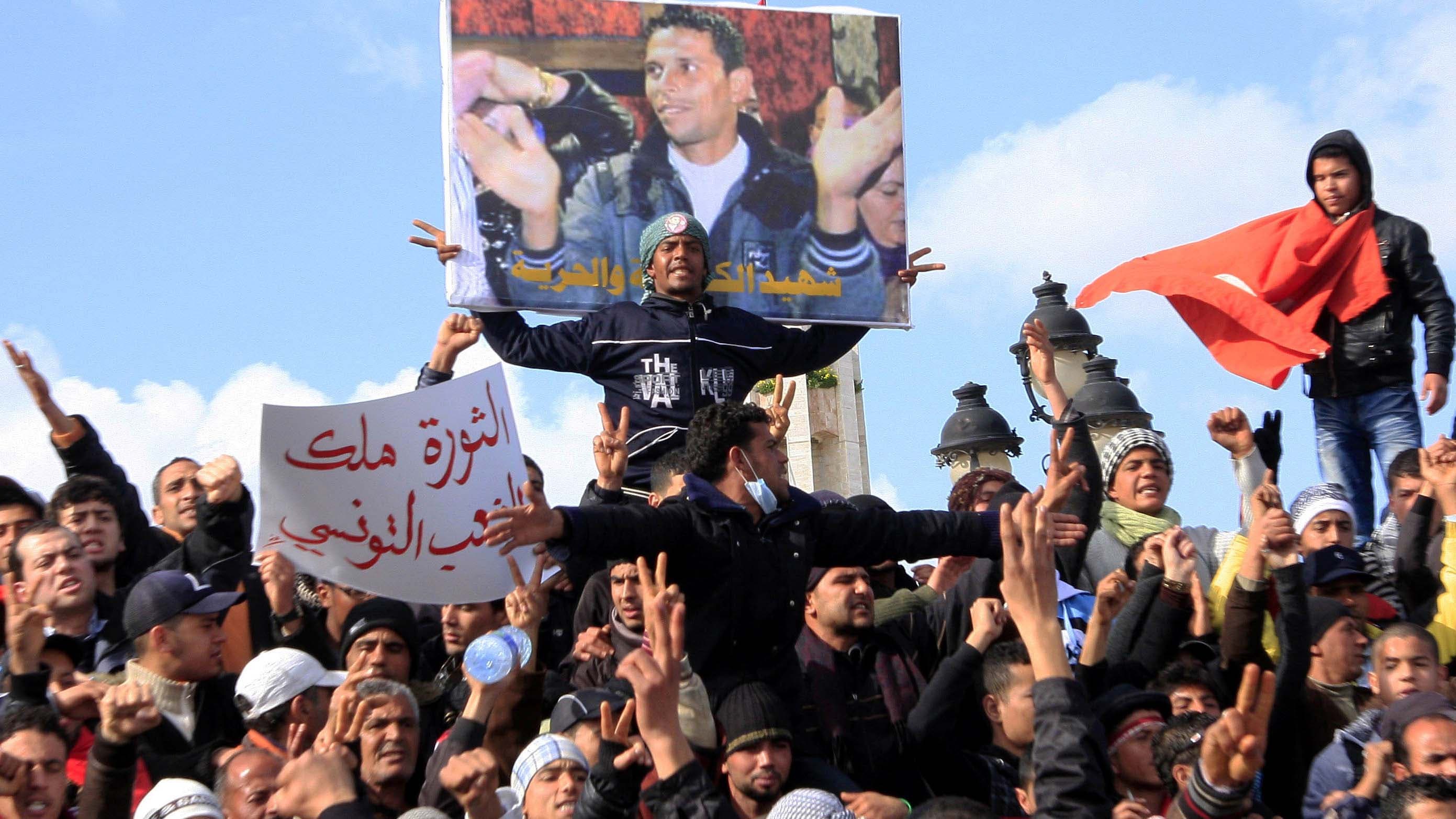 Tunisian protesters demonstrate beneath a poster of Mohamed Bouazizi near the prime minister's office in Tunis, Tunisia, Jan. 28, 2011.