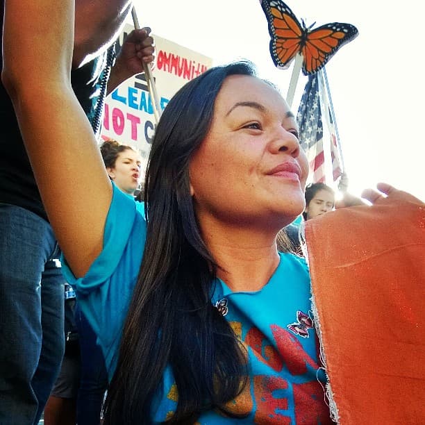 A woman wearing a blue shirt stands with a hand up and a monarch butterfly image near her.