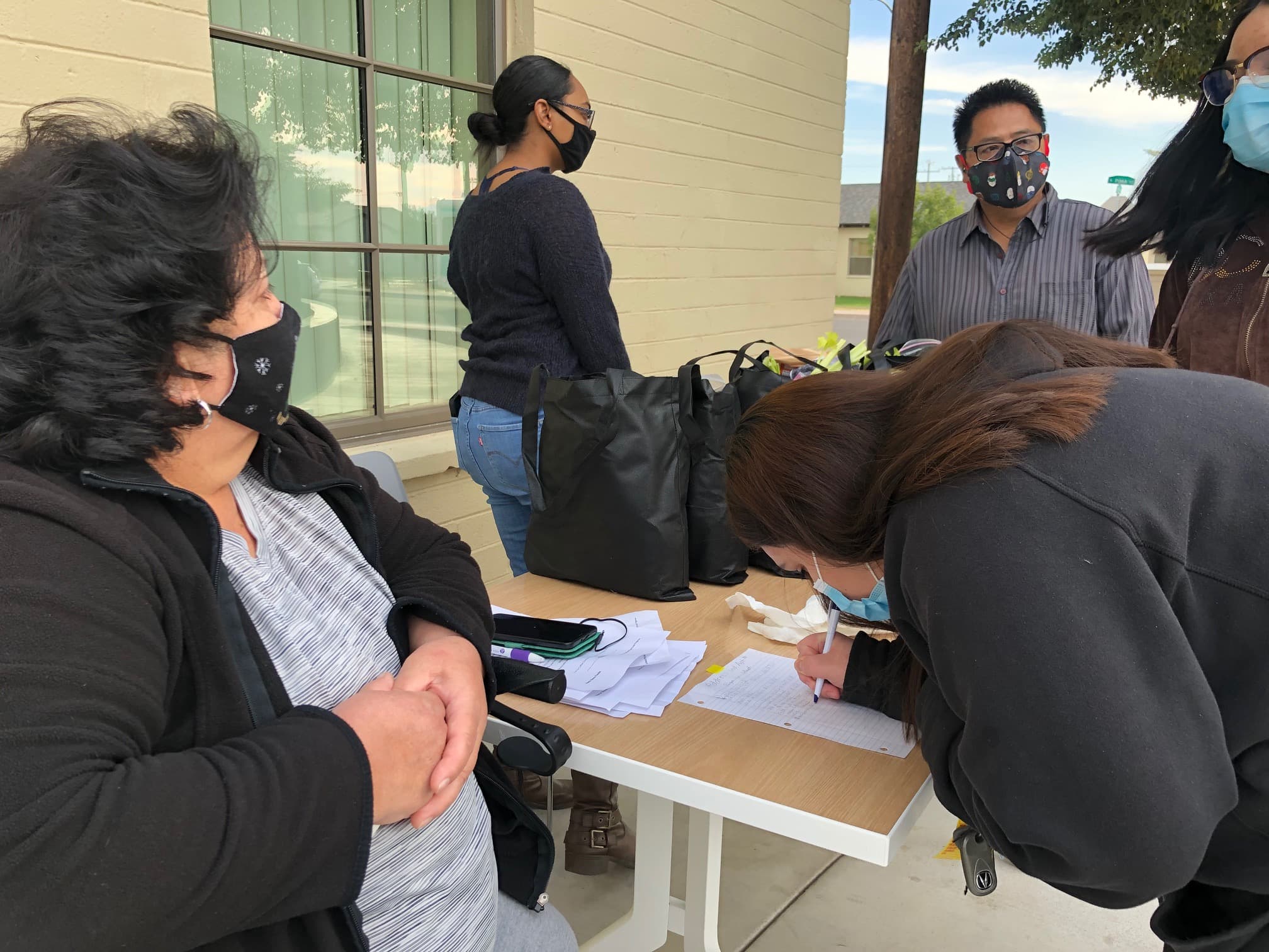 Several people wearing black clothes prepare food packages at a table.