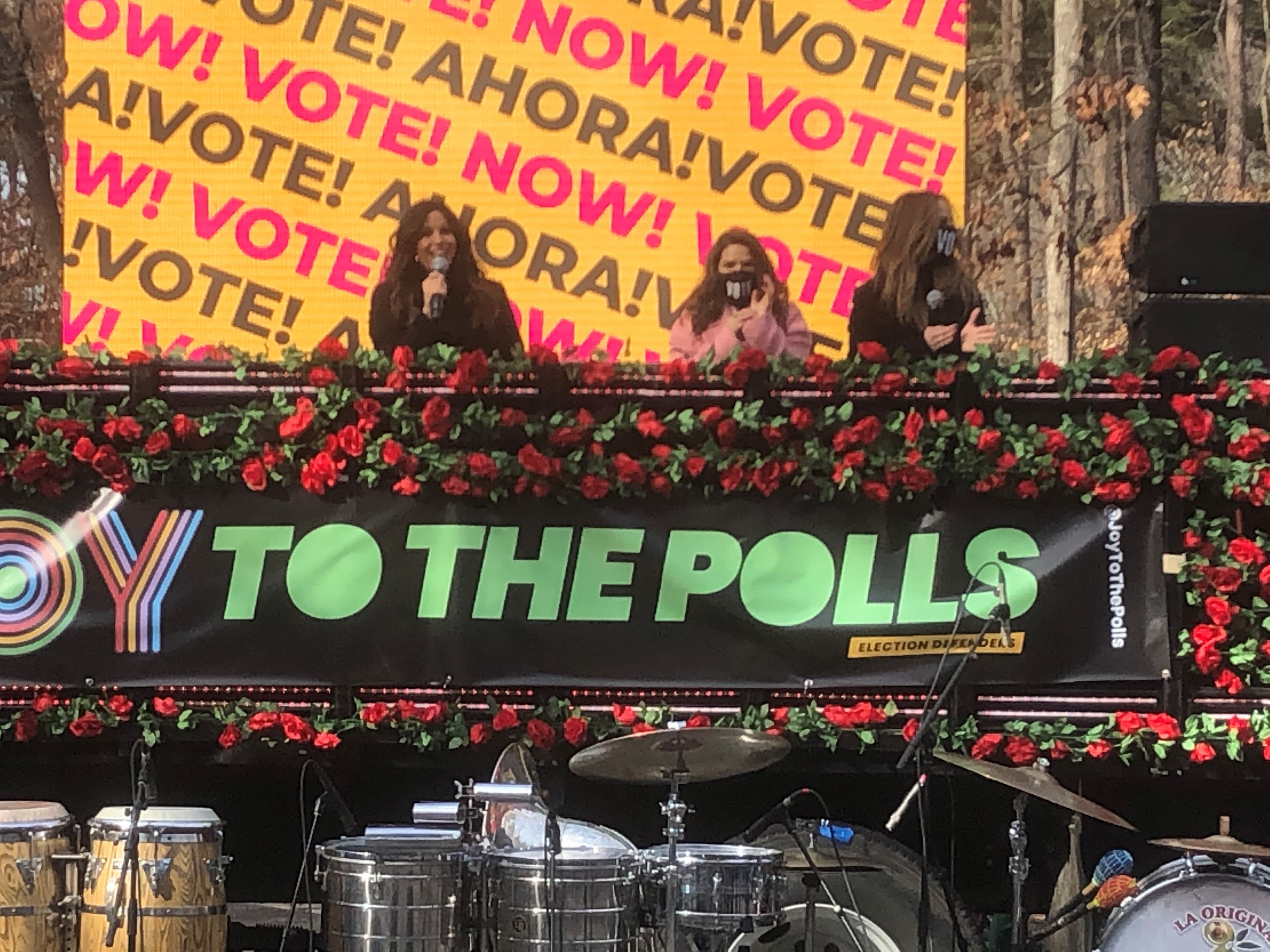 Actors sit on a panel in front of a large yellow and red sign that says vote.