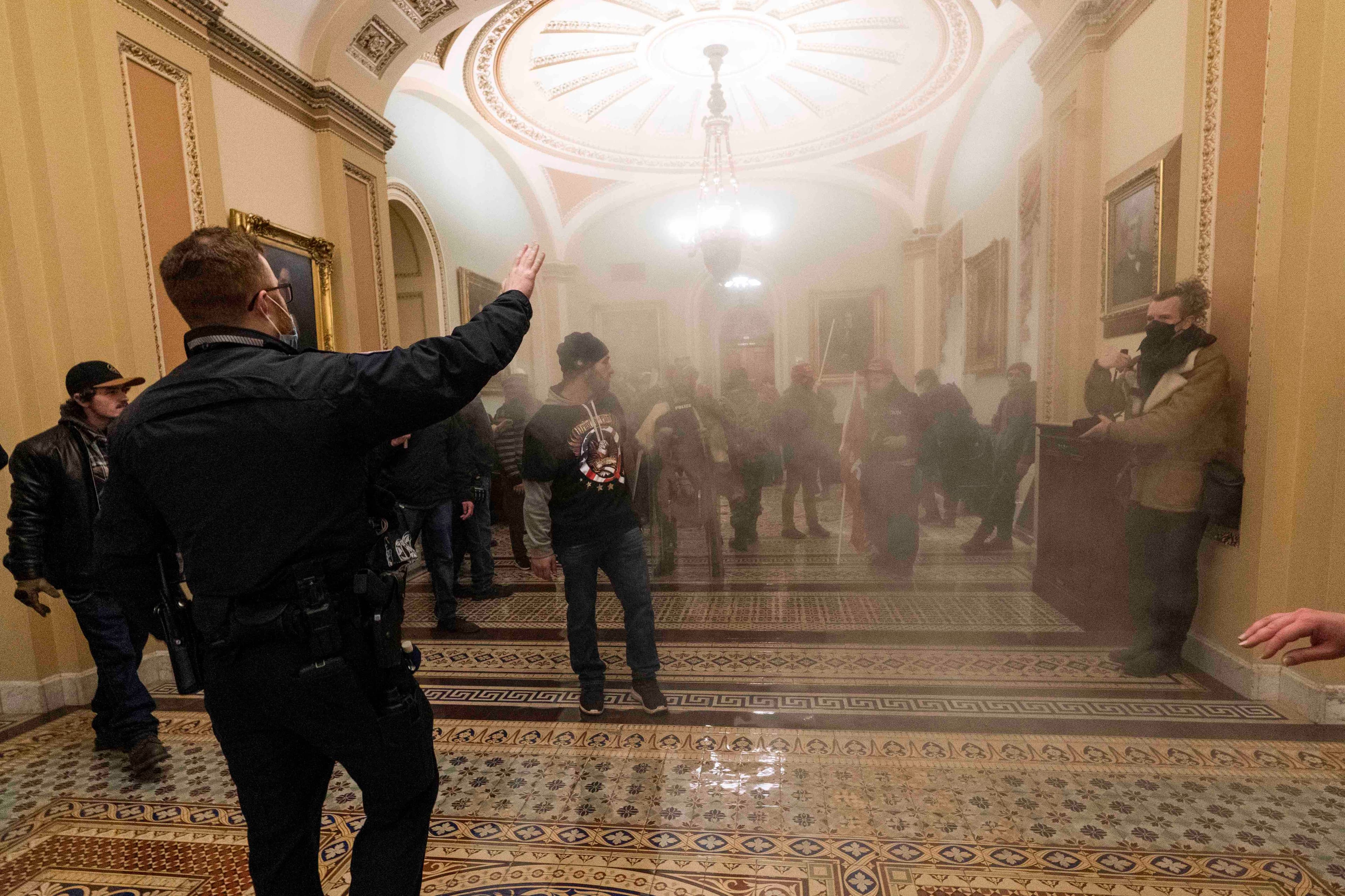 Smoke fills the walkway outside the Senate chamber as supporters of President Donald Trump are confronted by US Capitol Police officers inside the Capitol, Wednesday, Jan. 6, 2021, in Washington, DC.