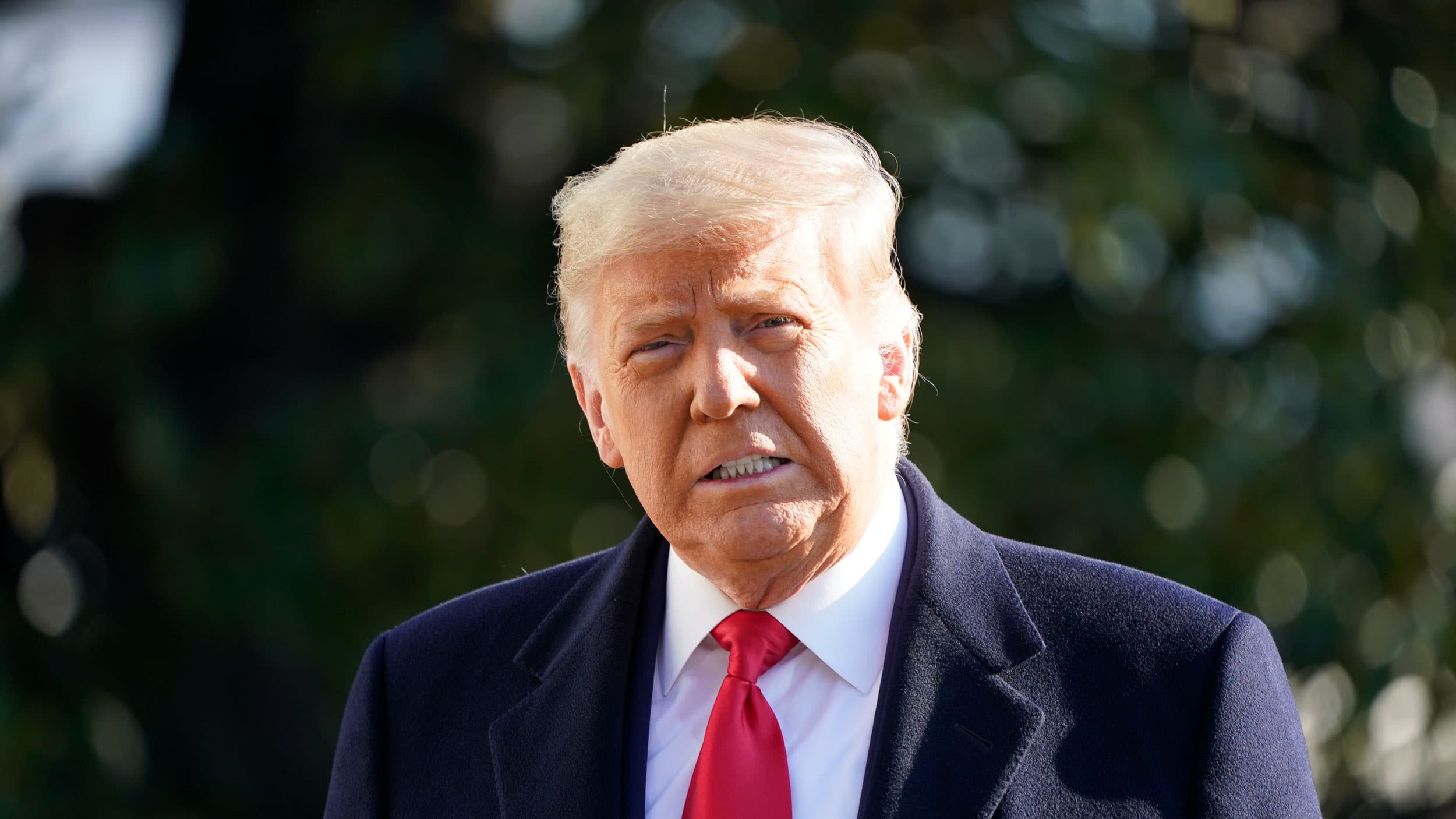 President Donald Trump is shown wearing a dark overcoat and read tie looking into the camera.
