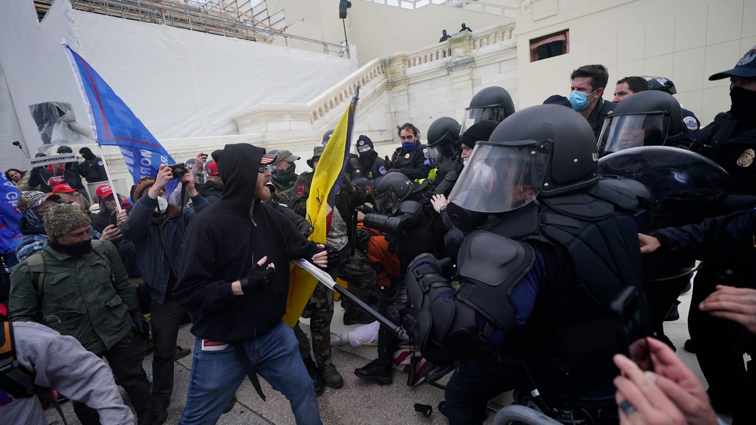 A large crowd of people are shown forcing their way past armed security officers at the US Capitol building.